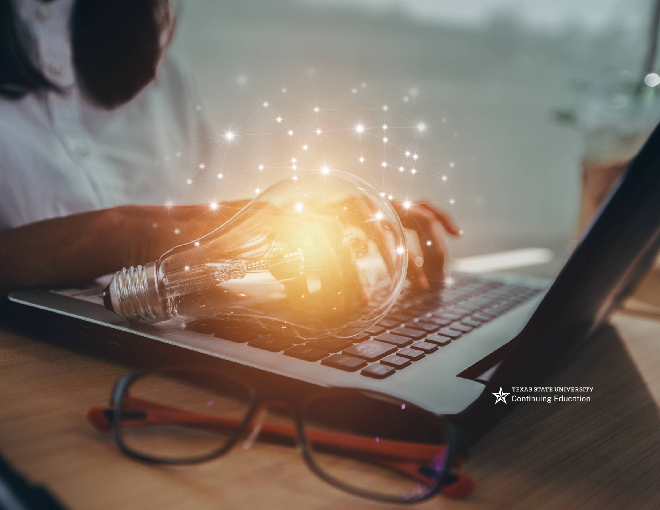 A seated woman typing on laptop with a metaphorical lightbulb on the keyboard