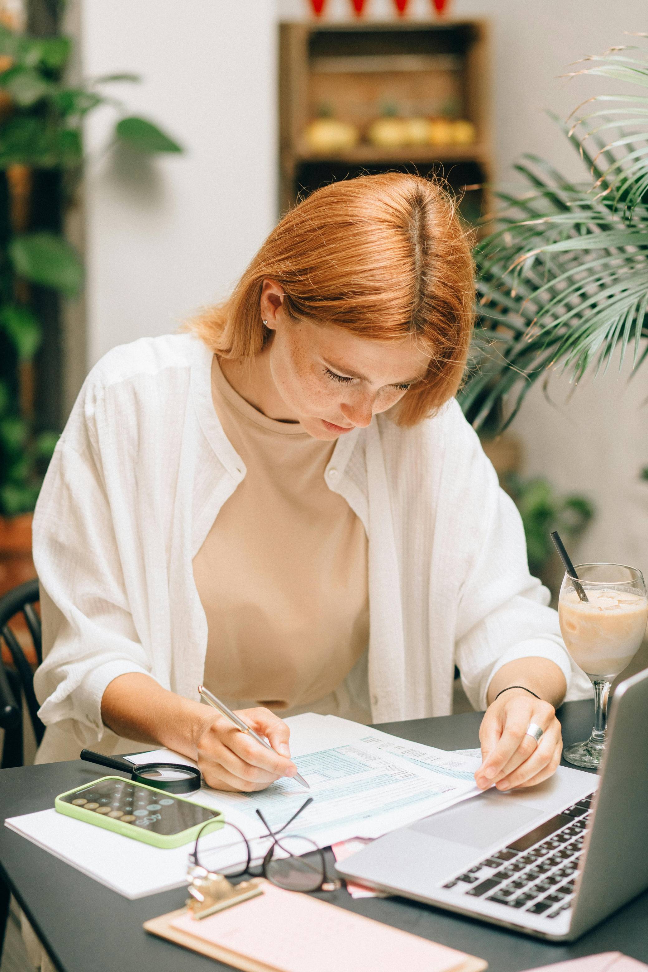 Small business owner reviews financial records beside a laptop and calculator, representing tax preparation and payroll responsibilities. The image supports a workshop on small business tax obligations, including worker classification, employee taxes, and independent contractor requirements.