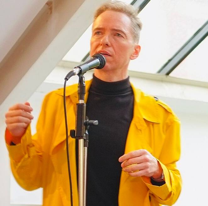 man in yellow jacket speaks into microphone
