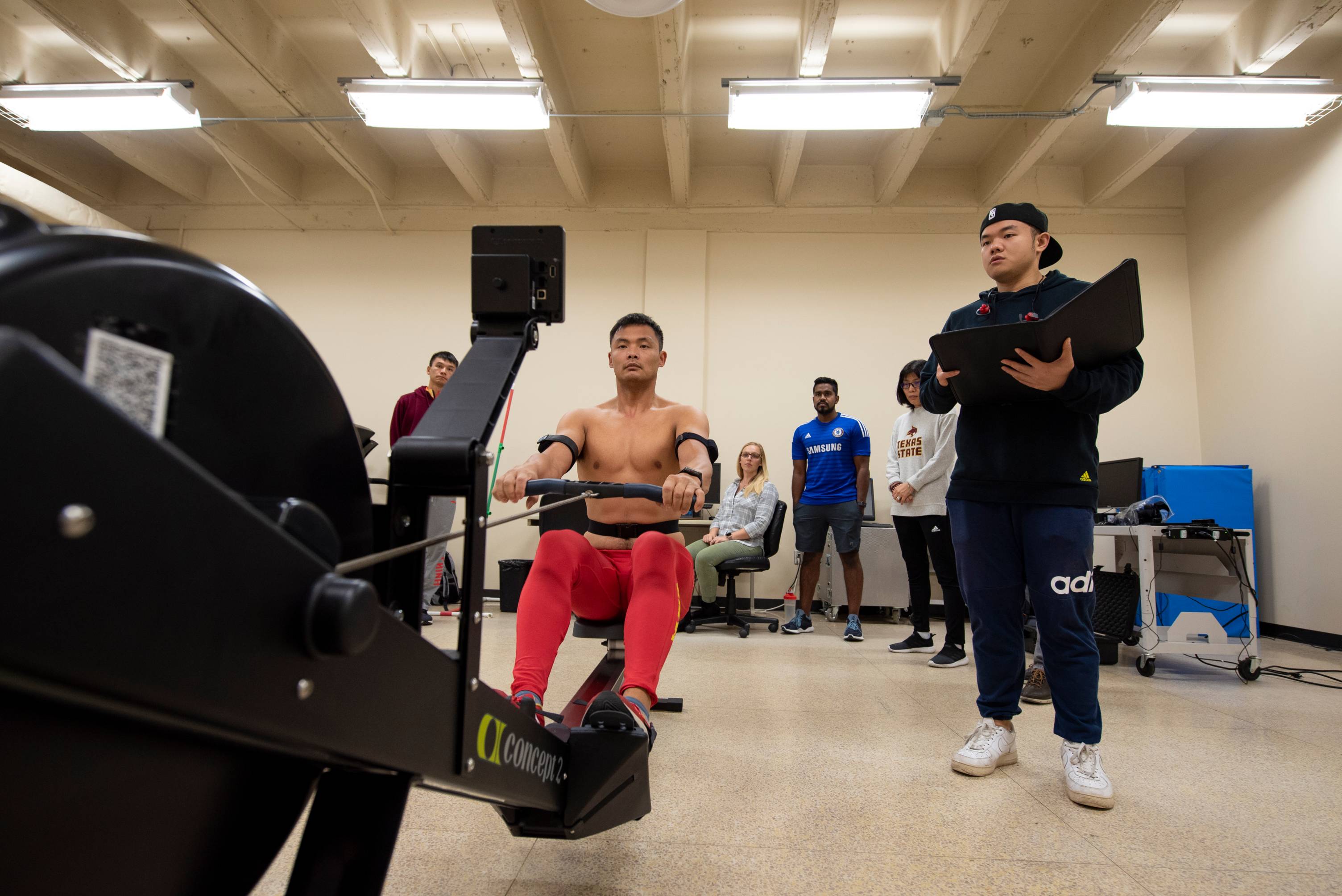 man exercises on rower while students observe