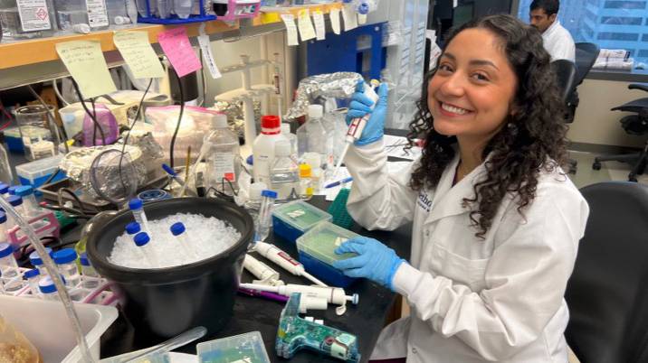 Patricia Garza poses for a photo while in a lab with a white coat.