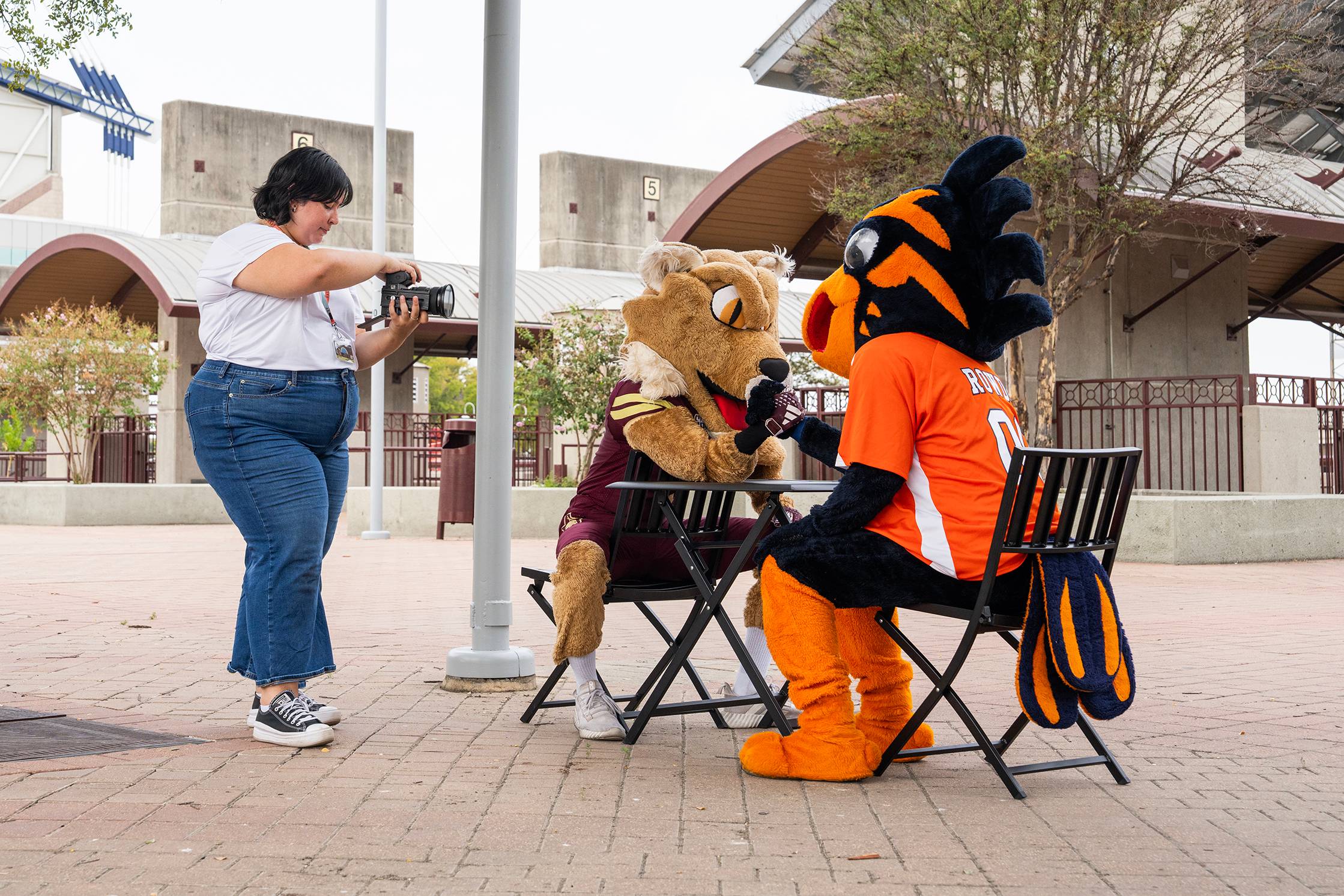 behind the scenes photo of a woman filming two mascots sitting at a table