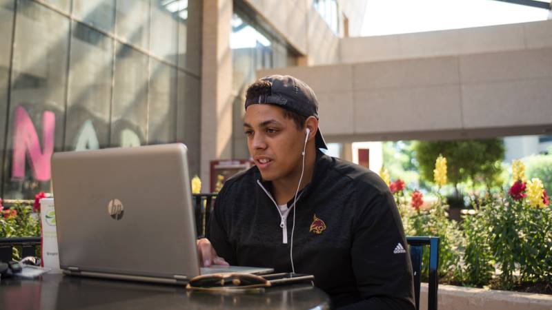 Student in front of a laptop sitting outside in a courtyard.