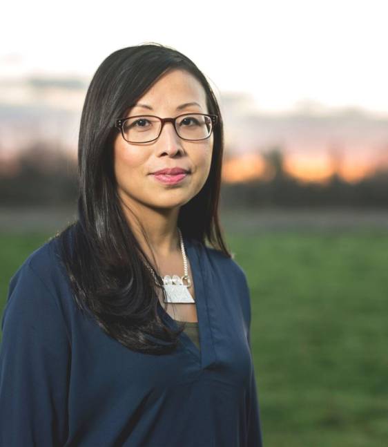 Headshot of a woman—author Mai Der Vang—standing in front of an outdoor landscape. 