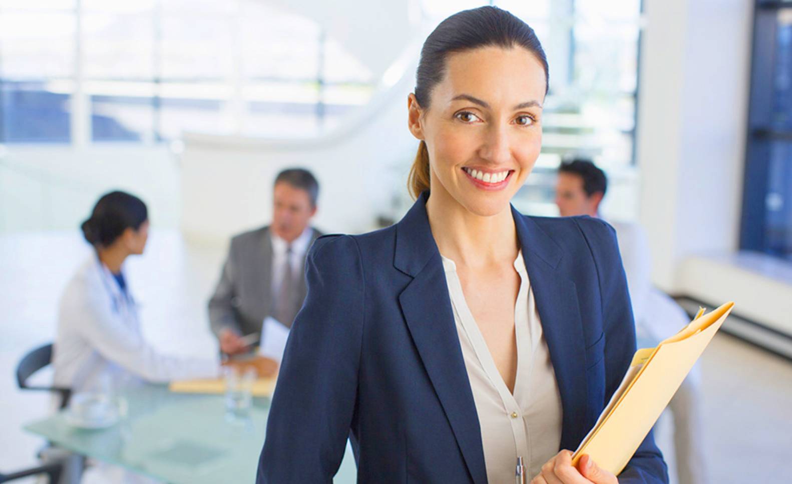 A female in slacks sitting behind a computer handing a woman a card.