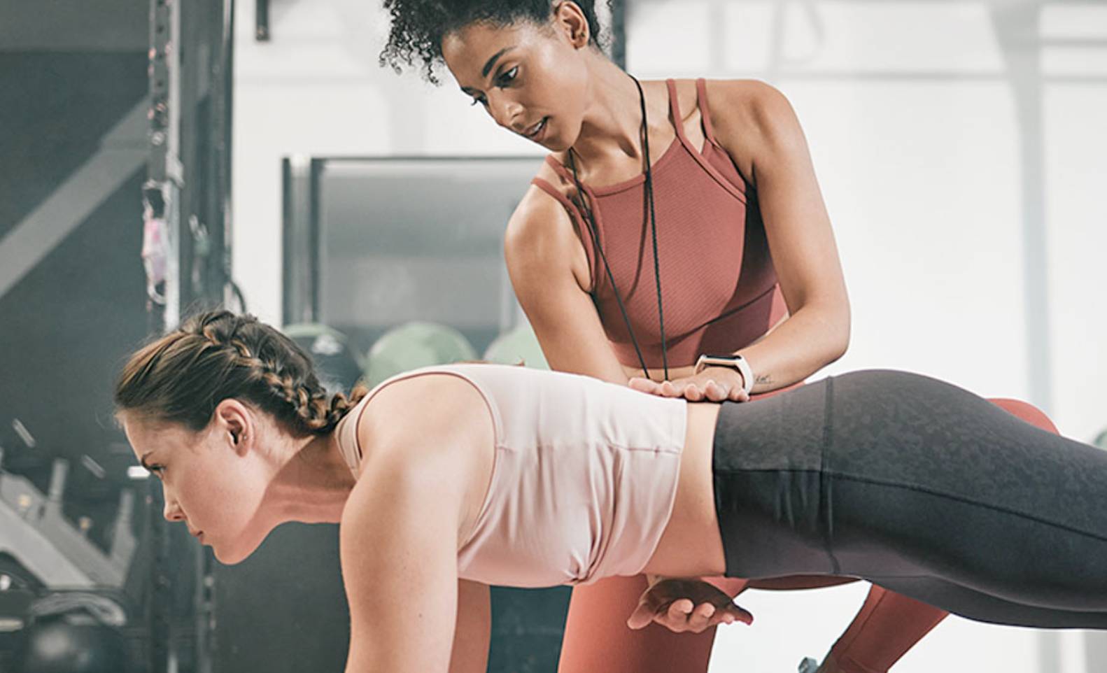 A woman doing sit-ups next to a personal trainer. 