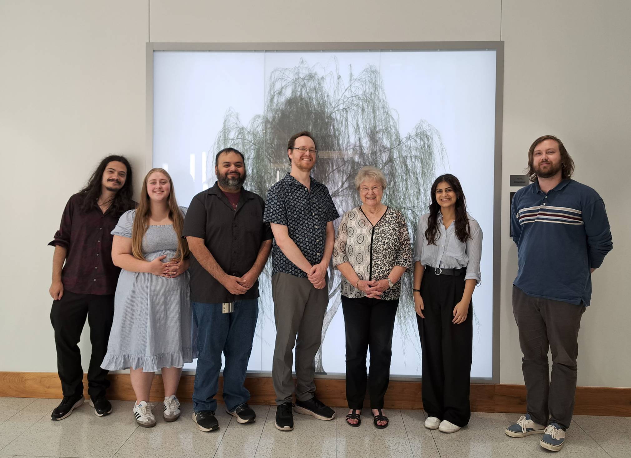 Staff members from Texas State University's University Advising Center pose for a picture in front of an image of a tree.