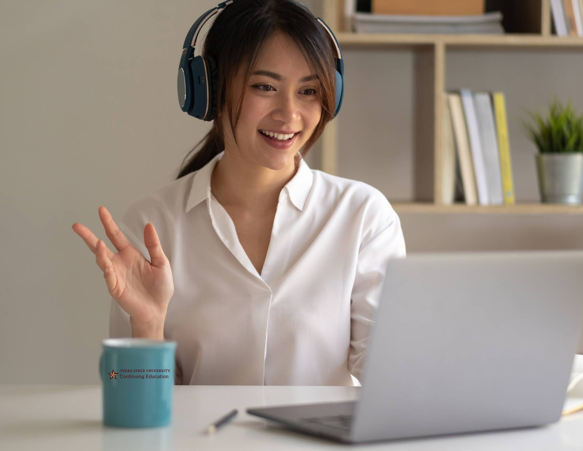 woman in headphones waving to her laptop screen