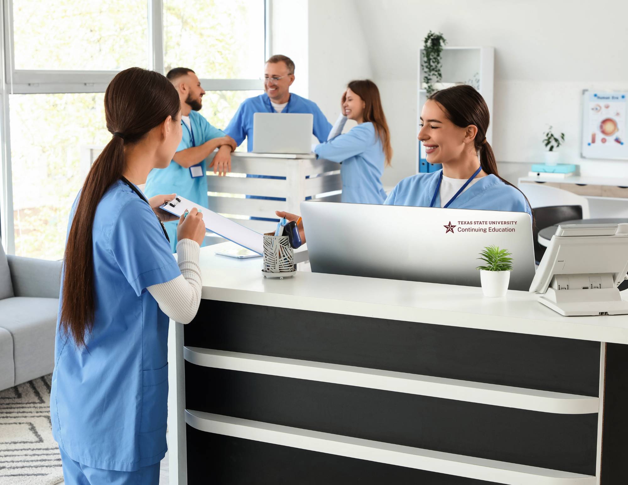 several nurses and doctors around the front desk in a hospital
