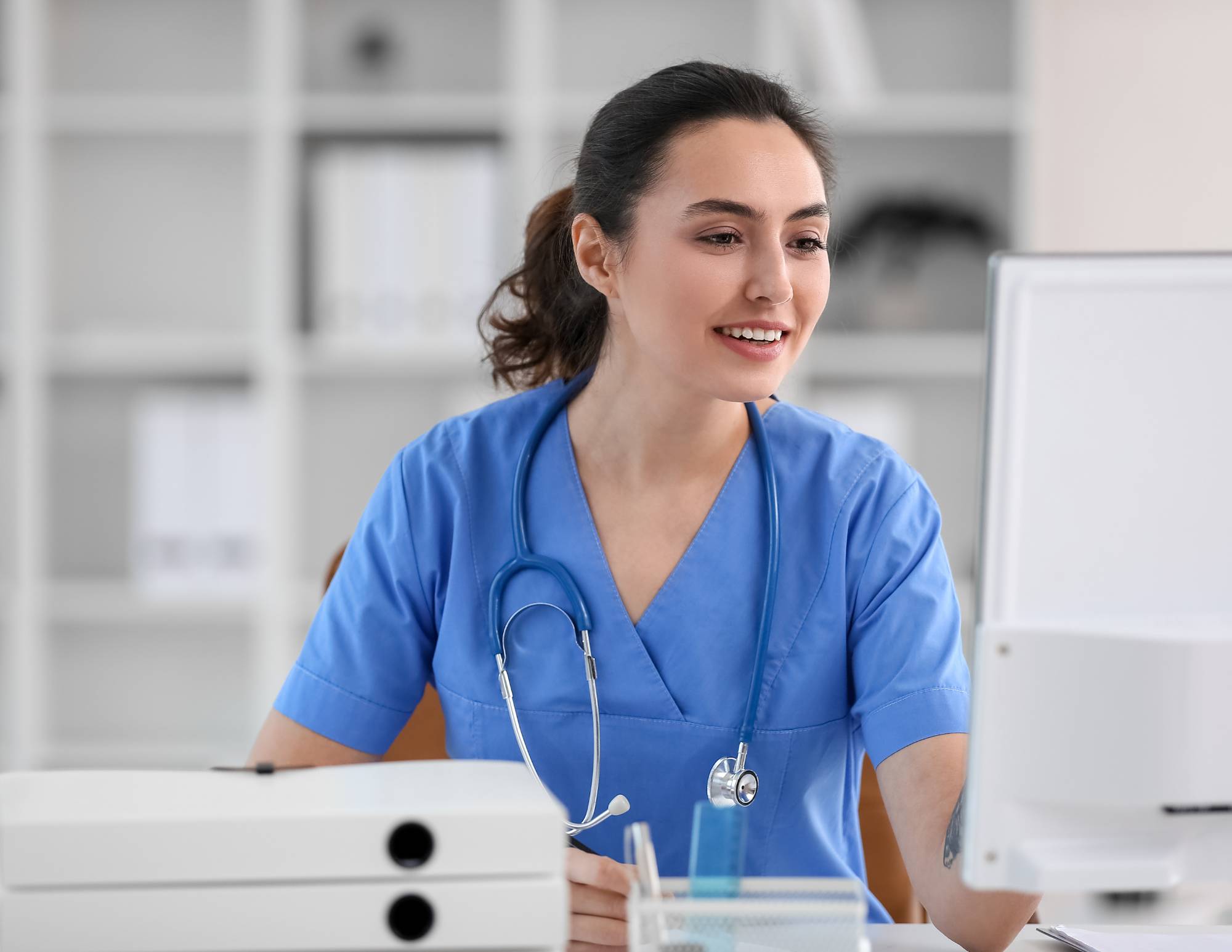 woman in scrubs with stethoscope on her neck reading computer screen