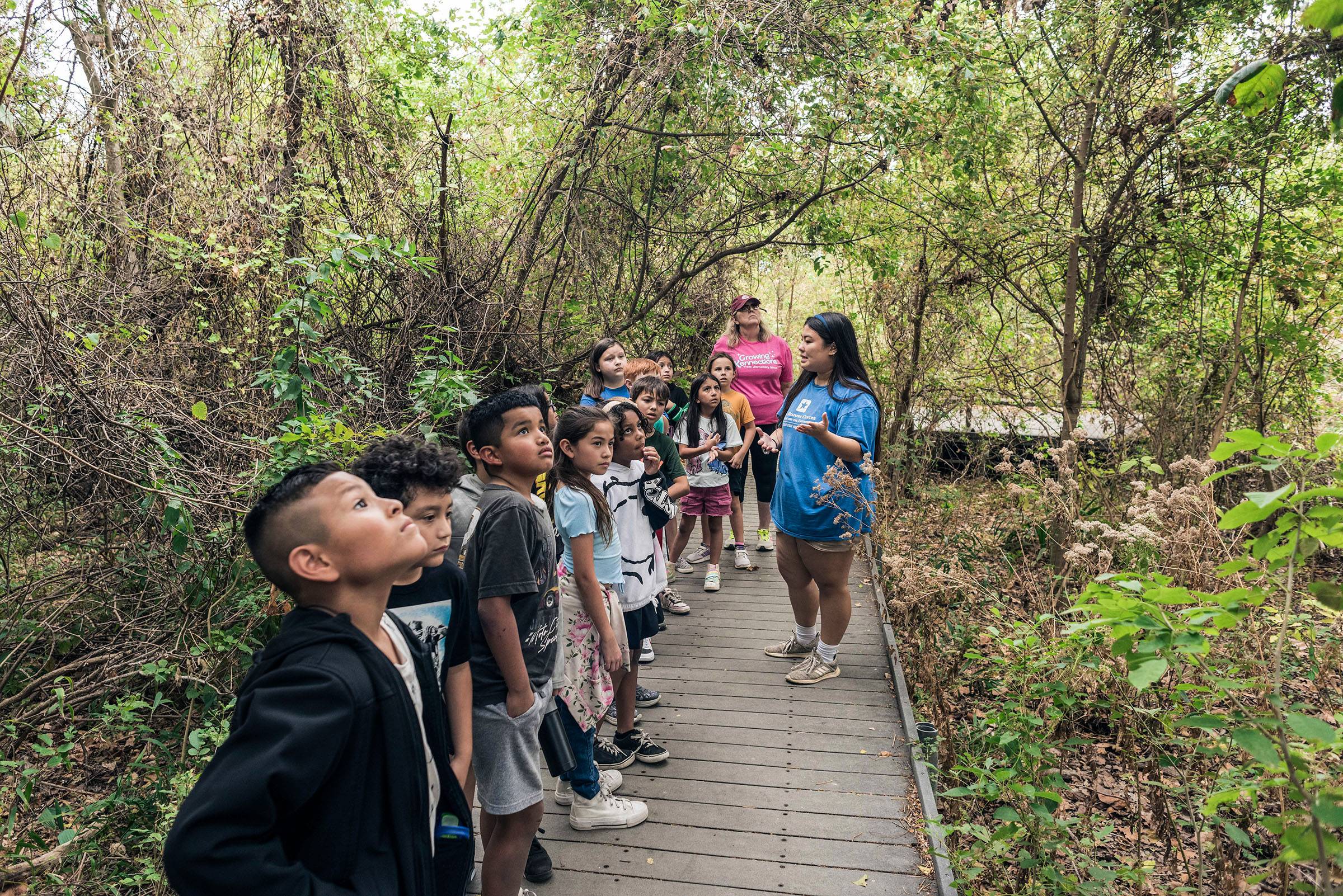 A group of children gathered a student worker giving a tour on the Wetlands Boardwalk at Spring Lake