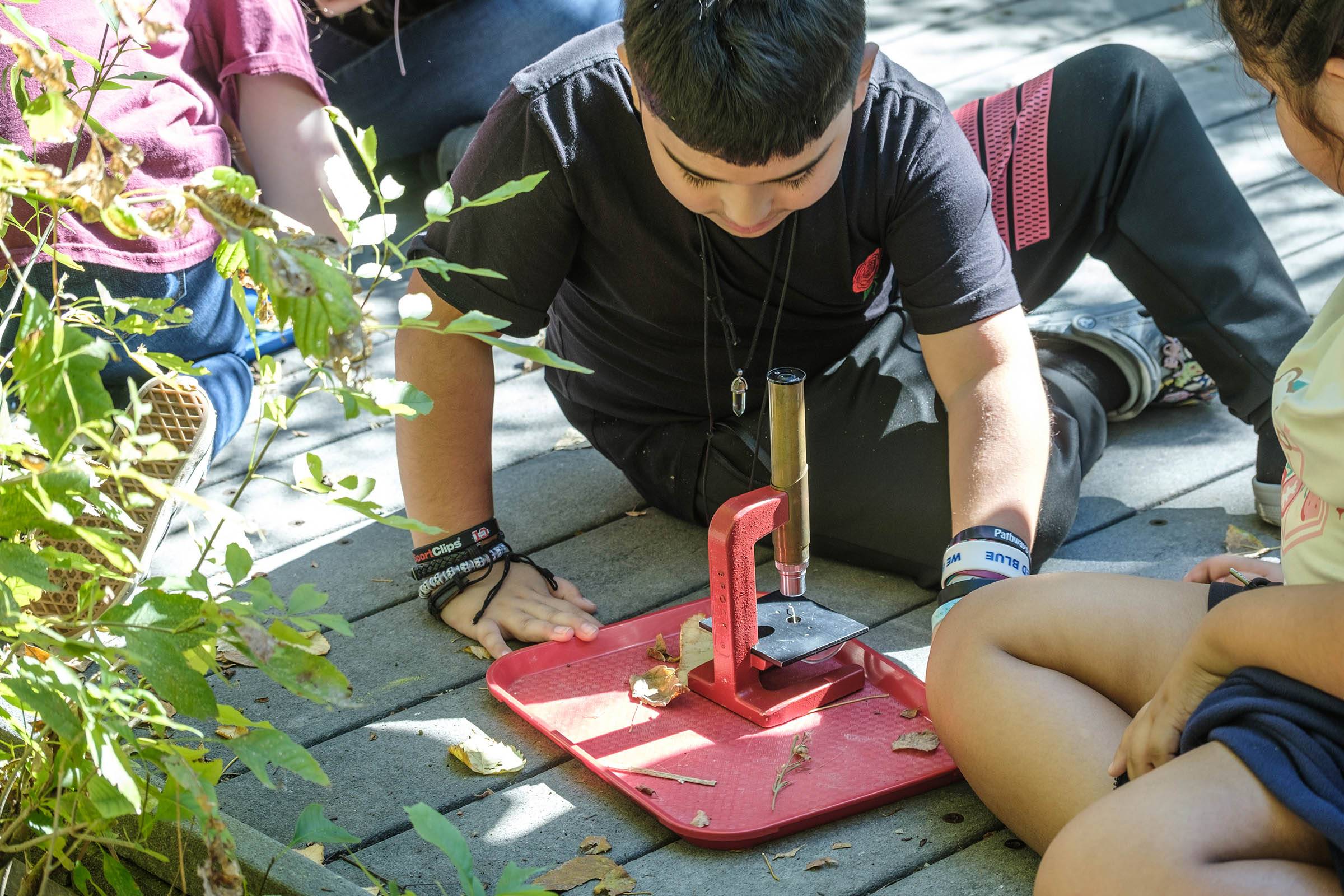 A boy kneeling on the ground looking at a microsope.