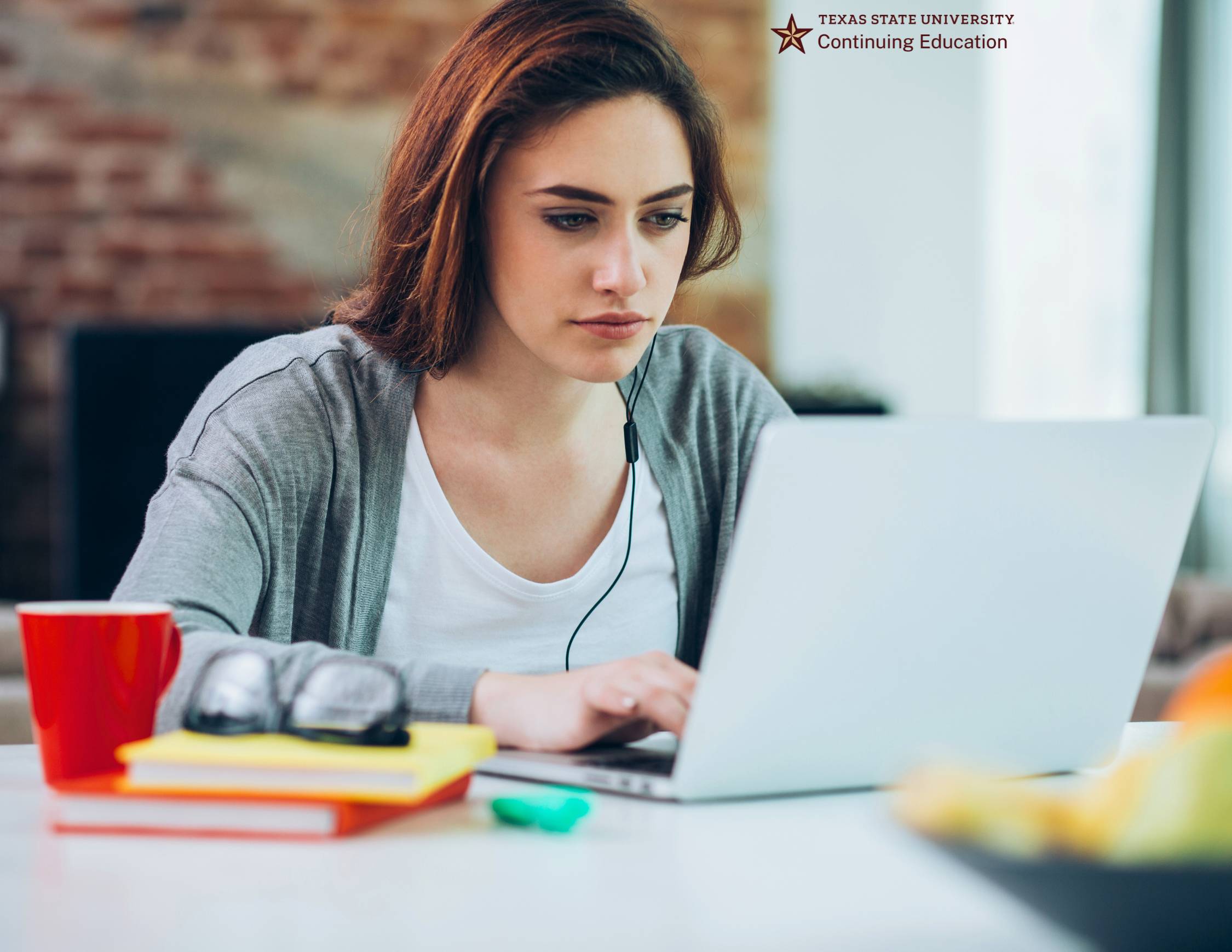 A woman sitting at a table with a red coffee cup engaged in an online course