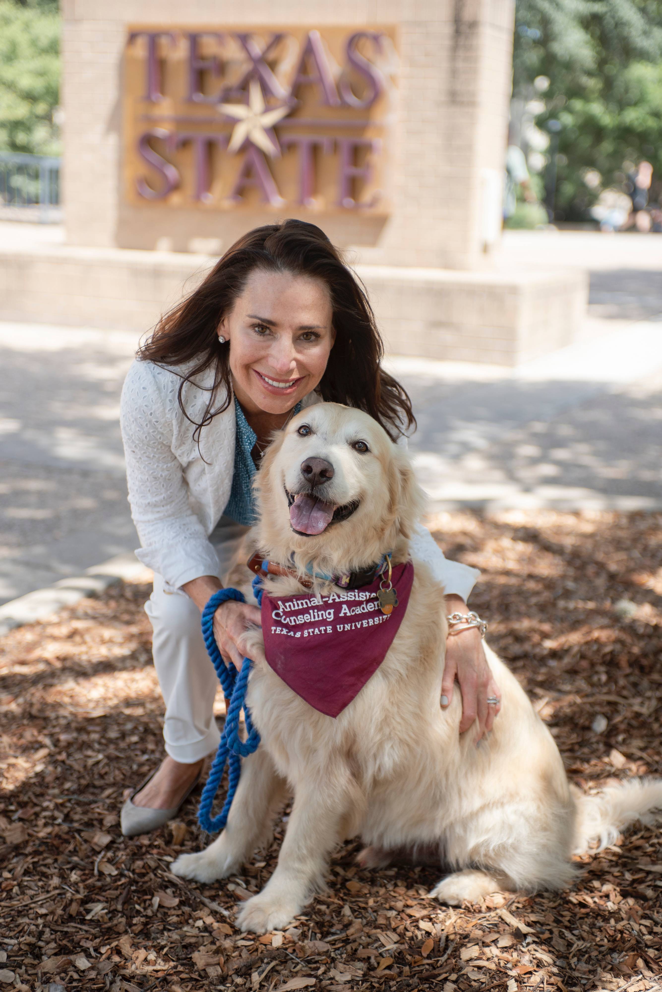 AAC practitioner and golden retriever in front of TXST sign
