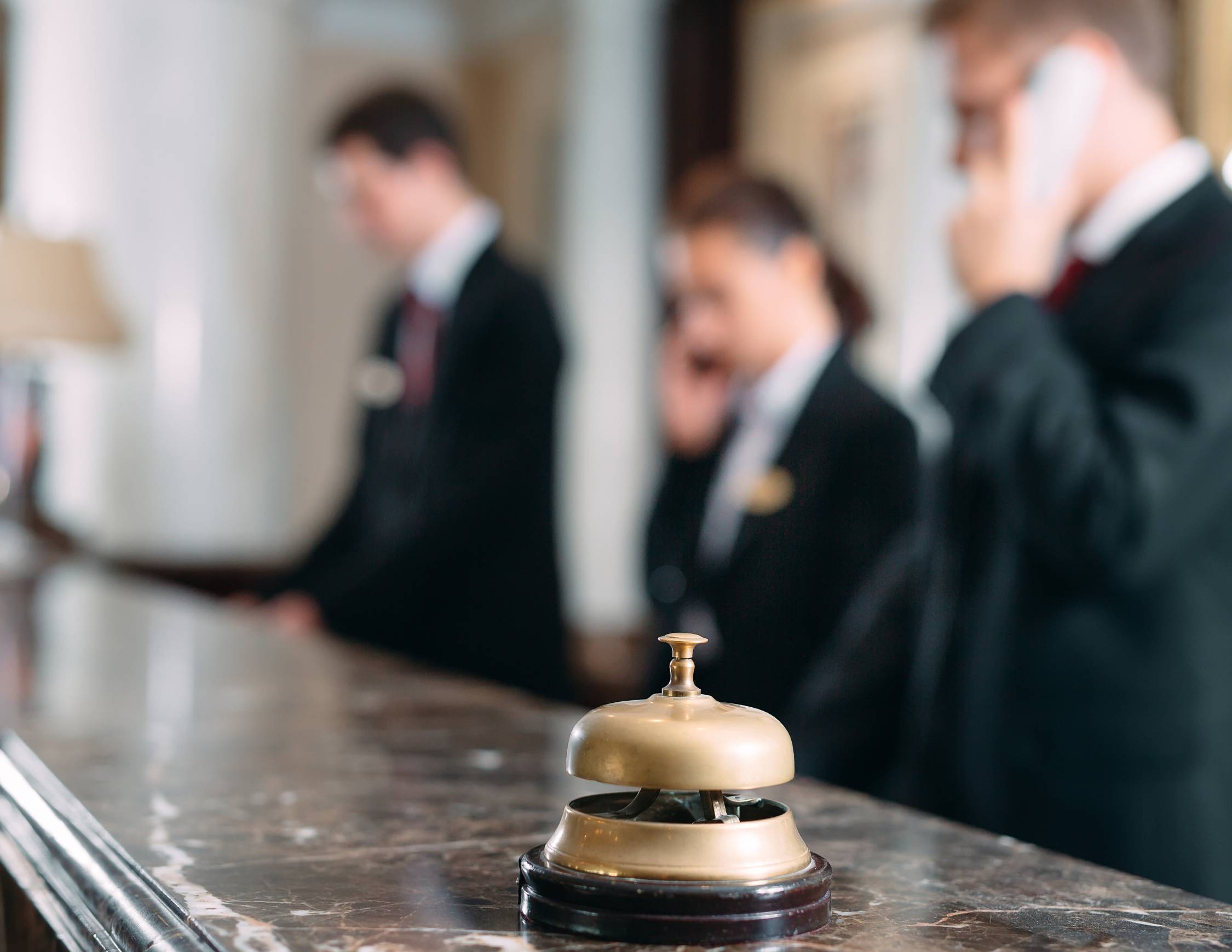 a bell on a marble desk with 3 blurred workers behind it