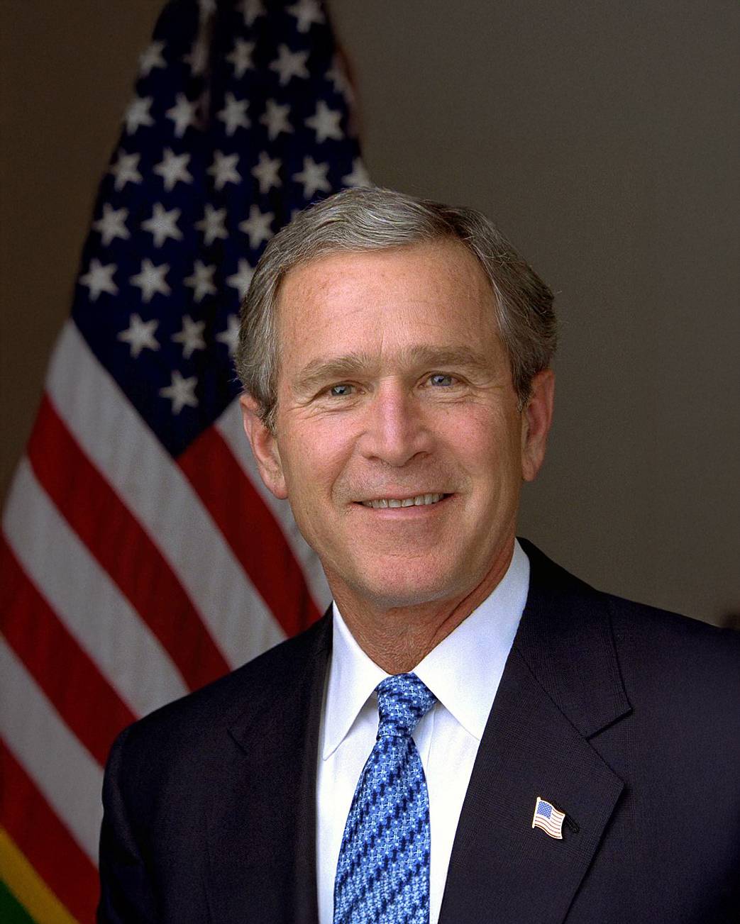 Man in suit with blue tie sits in front of American flag