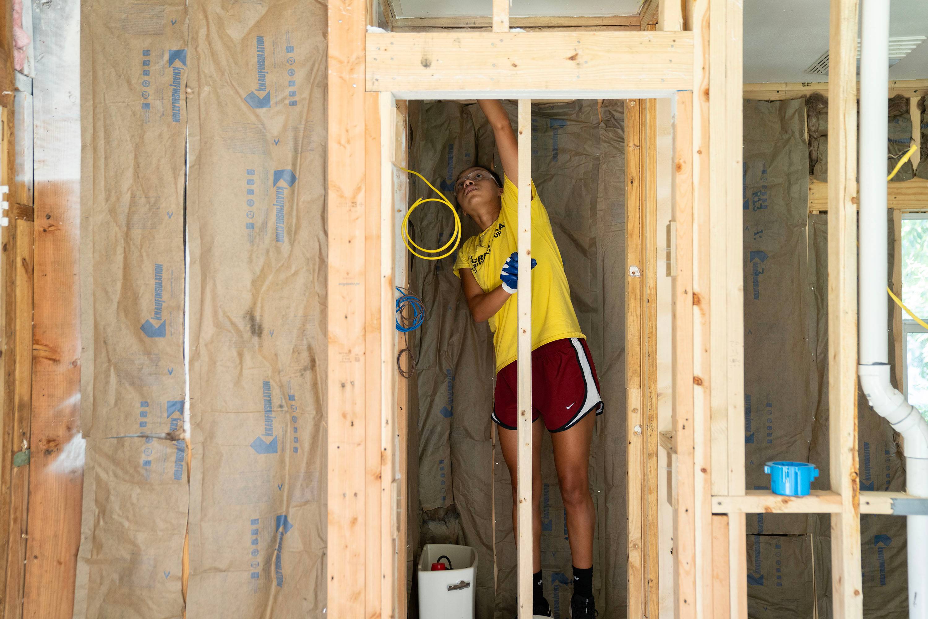 A student works on a door frame in a room with exposed studs.