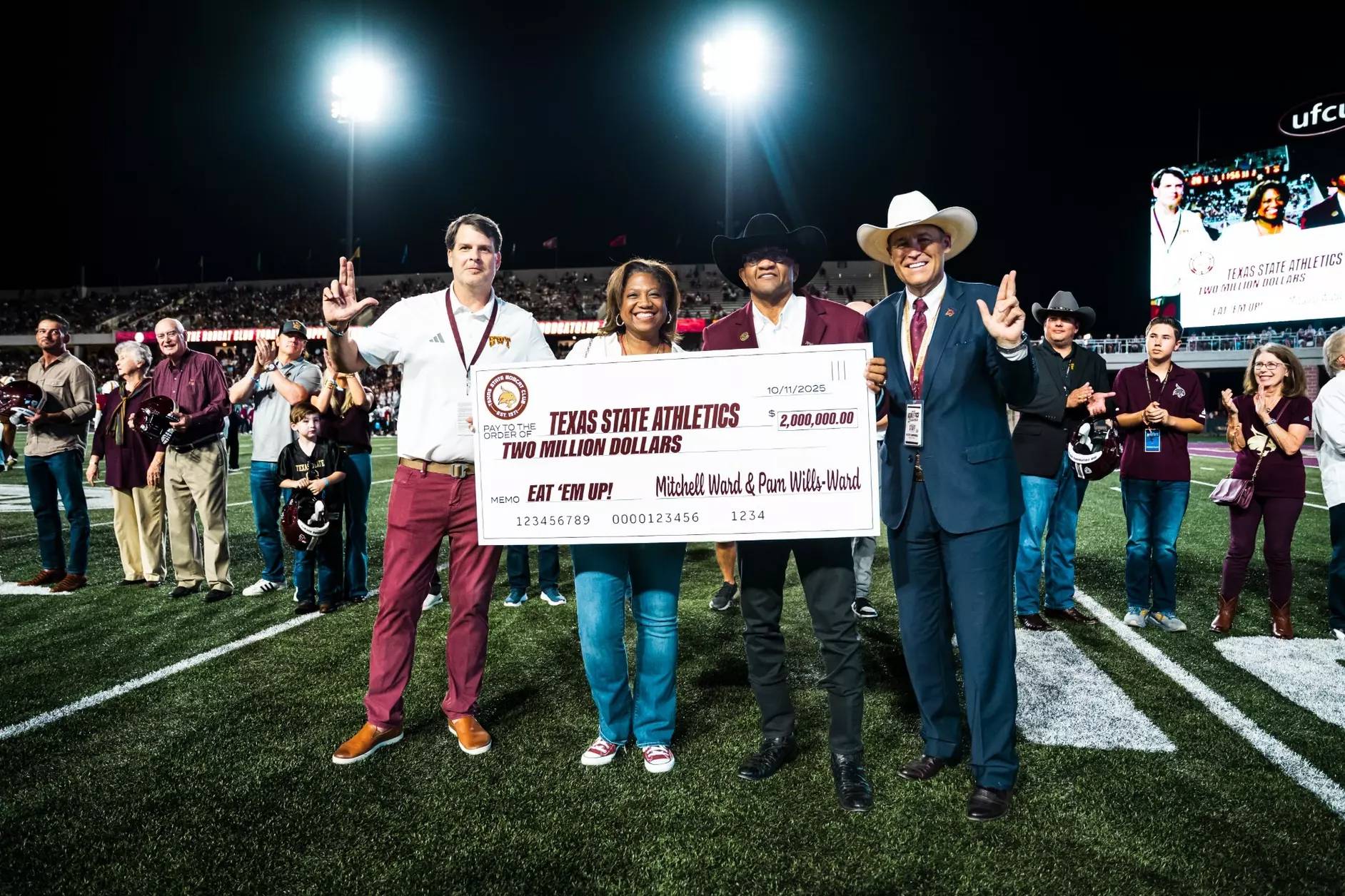 four people holding up large donation check on football field