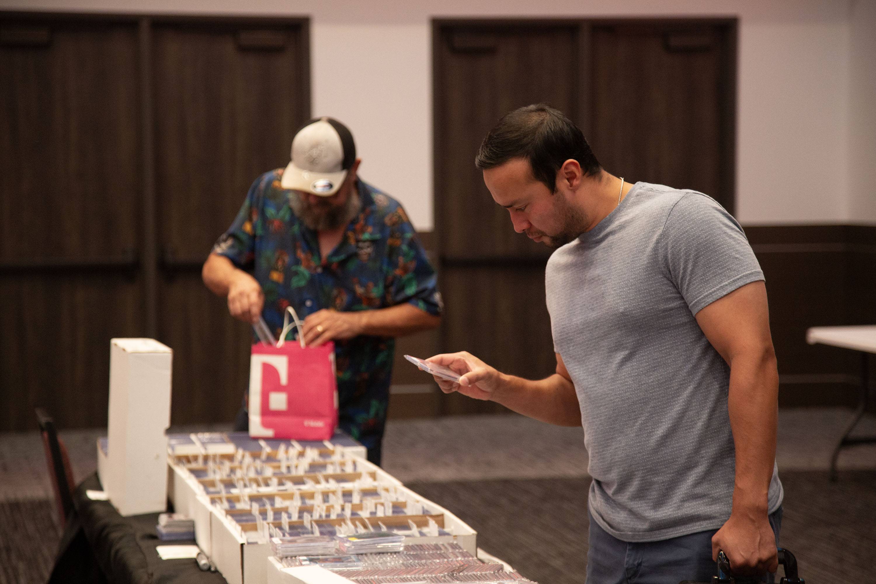 A man in a gray shirt holds and looks at a trading card in his hand.