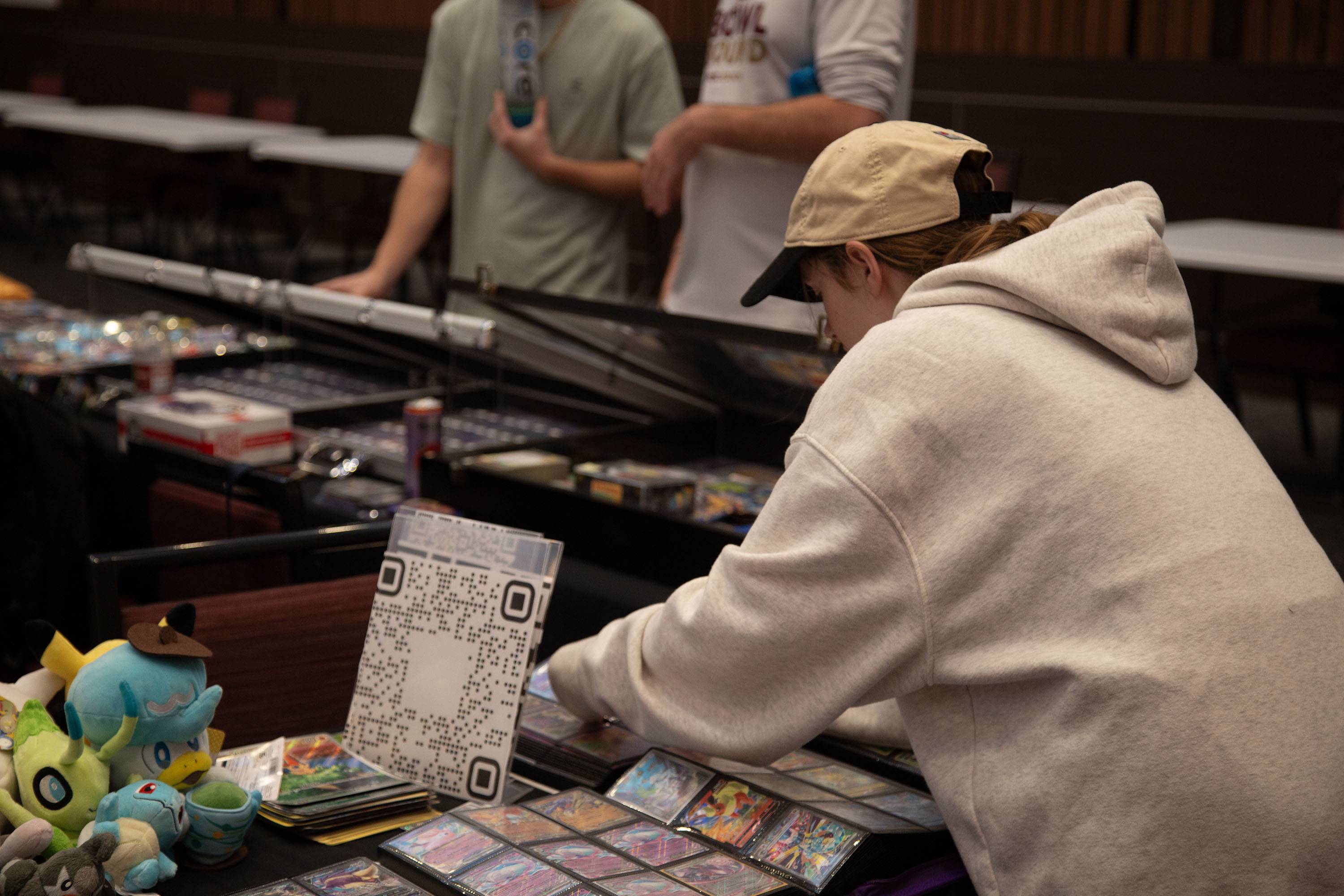student in beige sweatshirt and hat looks at trading cards on a table