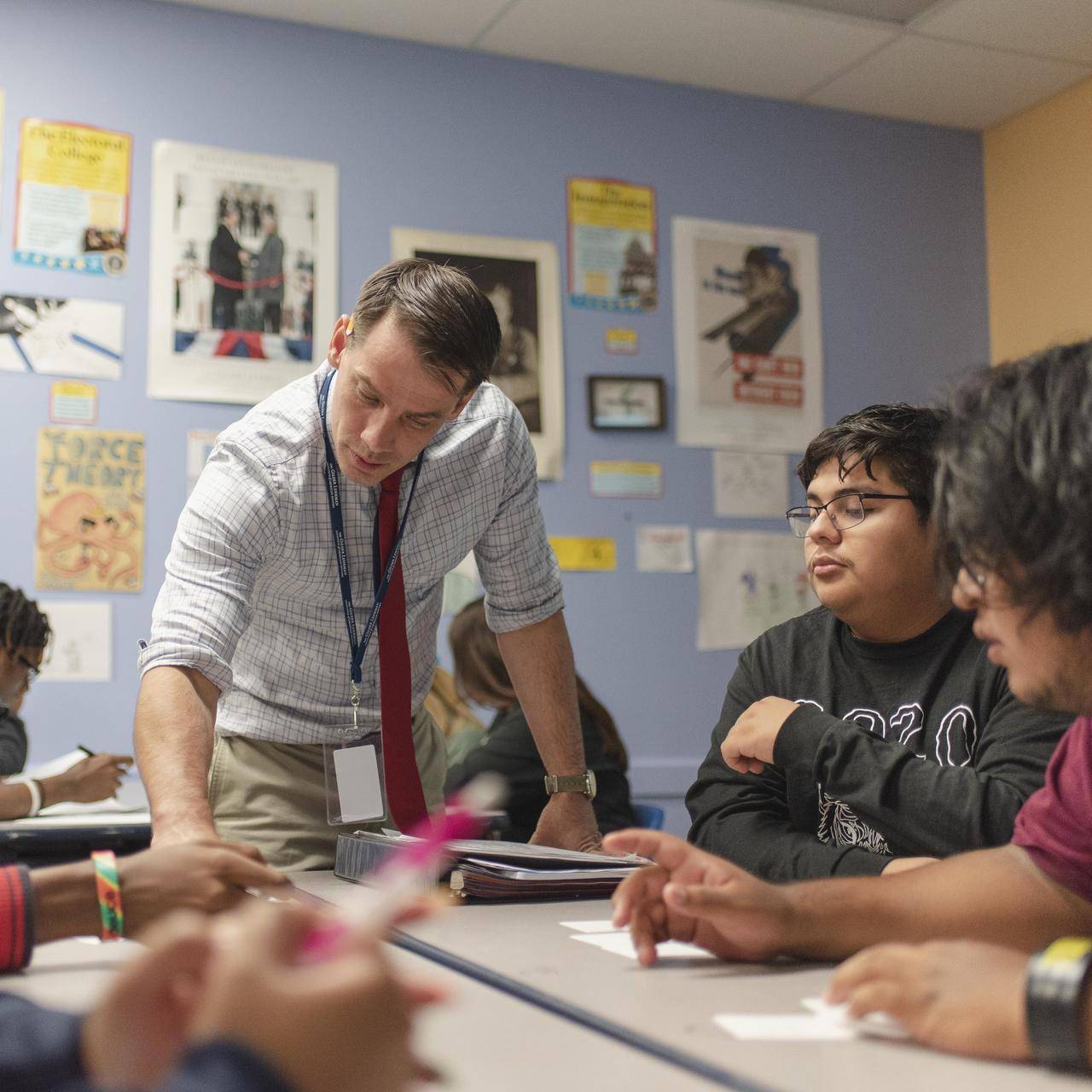 A high school teacher shows a small group of students some instructions on a piece of paper.