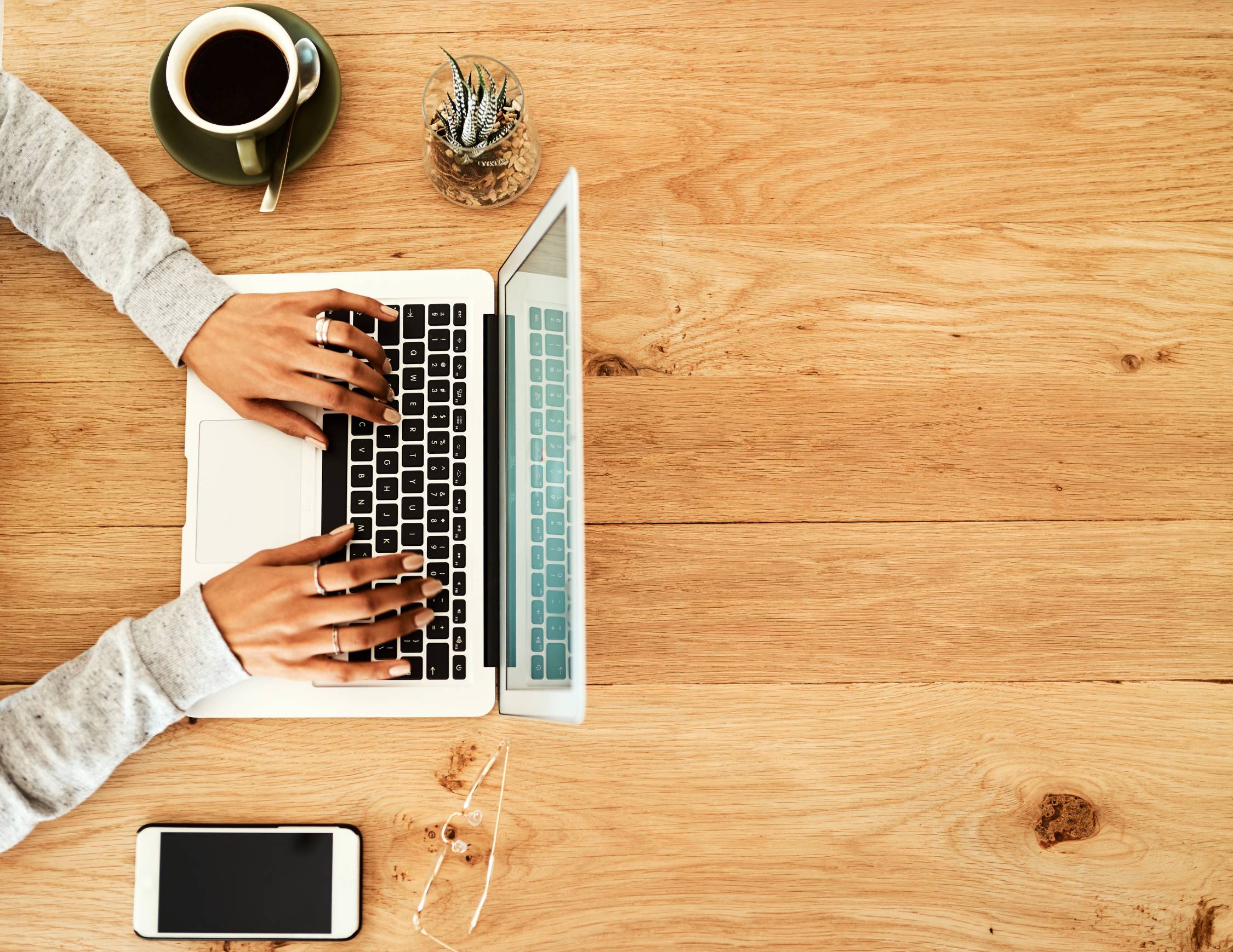 a woman typing on a laptop sitting on a wood table