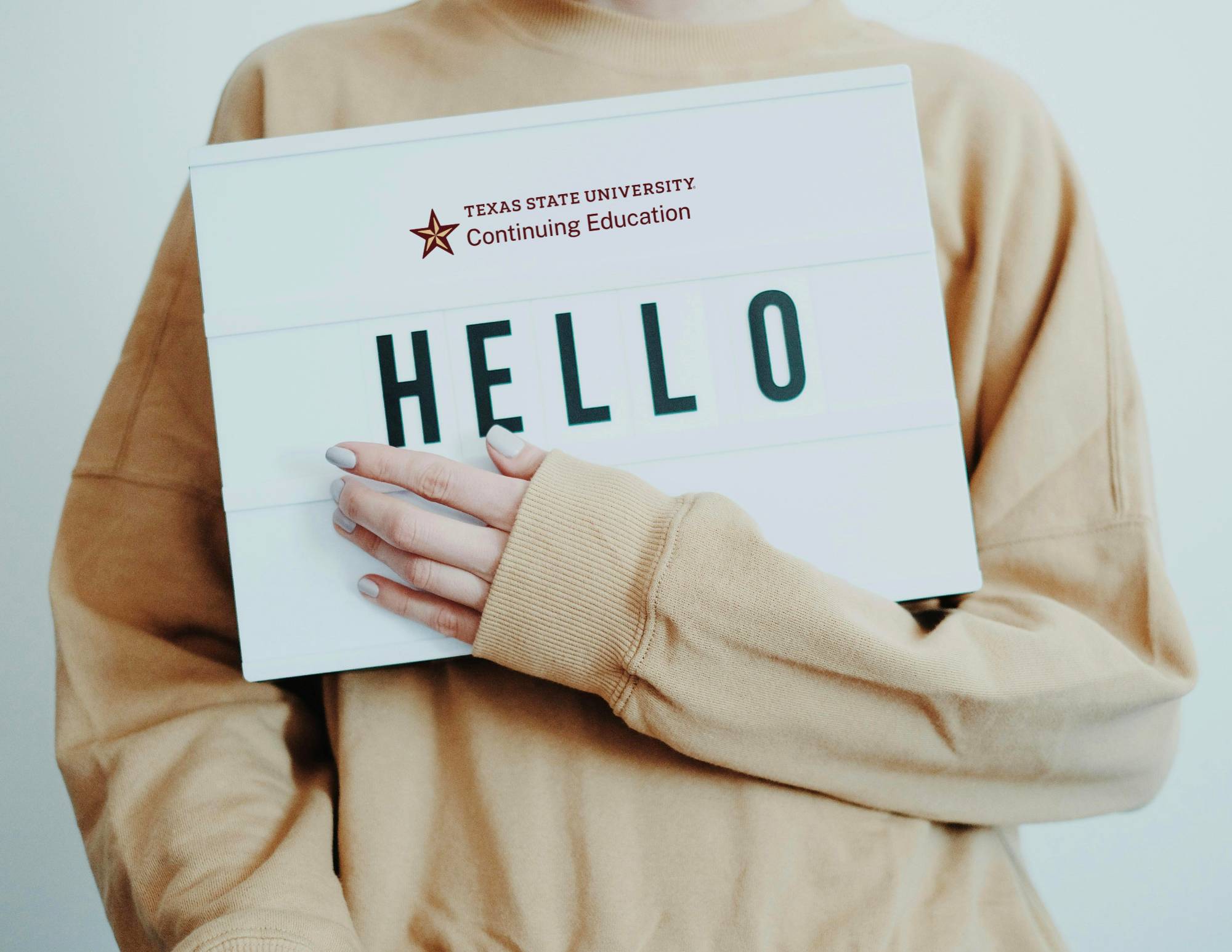 a woman in beige sweater with blue nails holding a sign which reads hello