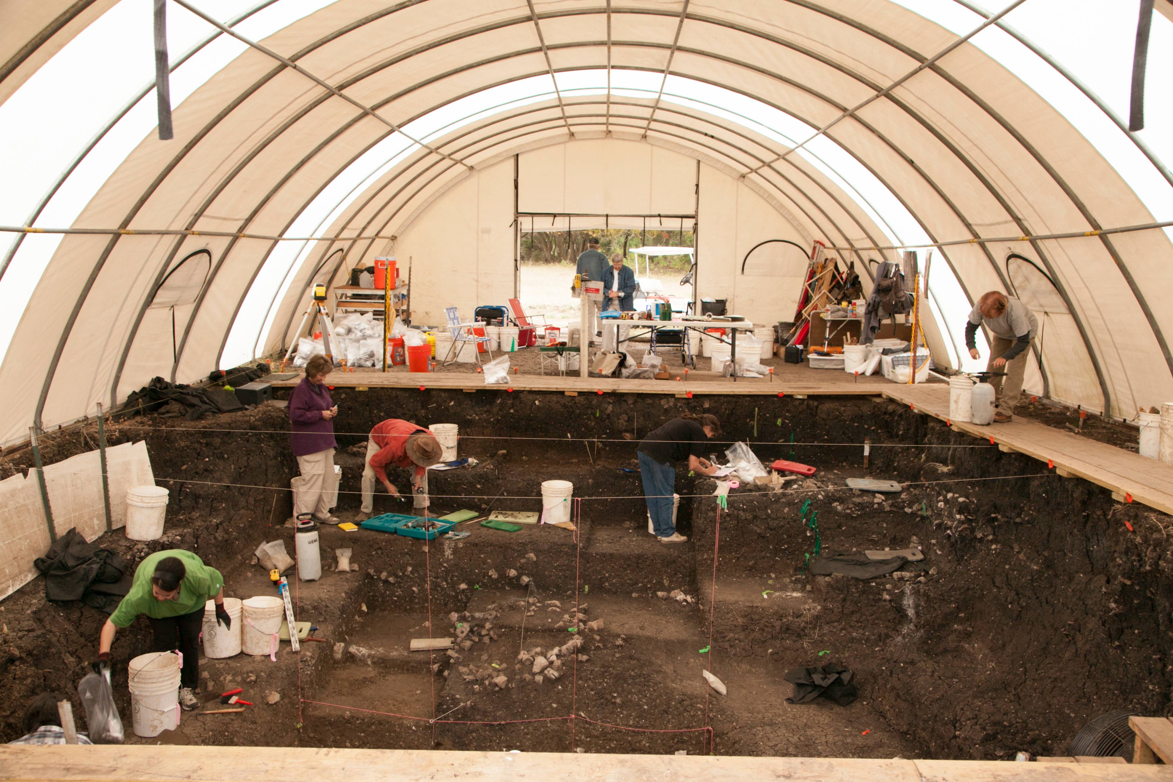 Archeological students work to uncover artifacts in dirt area.