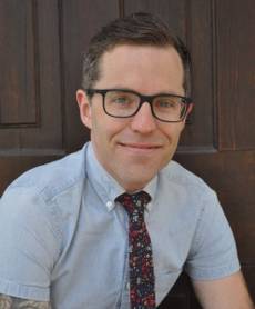 man with glasses wearing a short sleeve button up shirt and tie smiling at camera