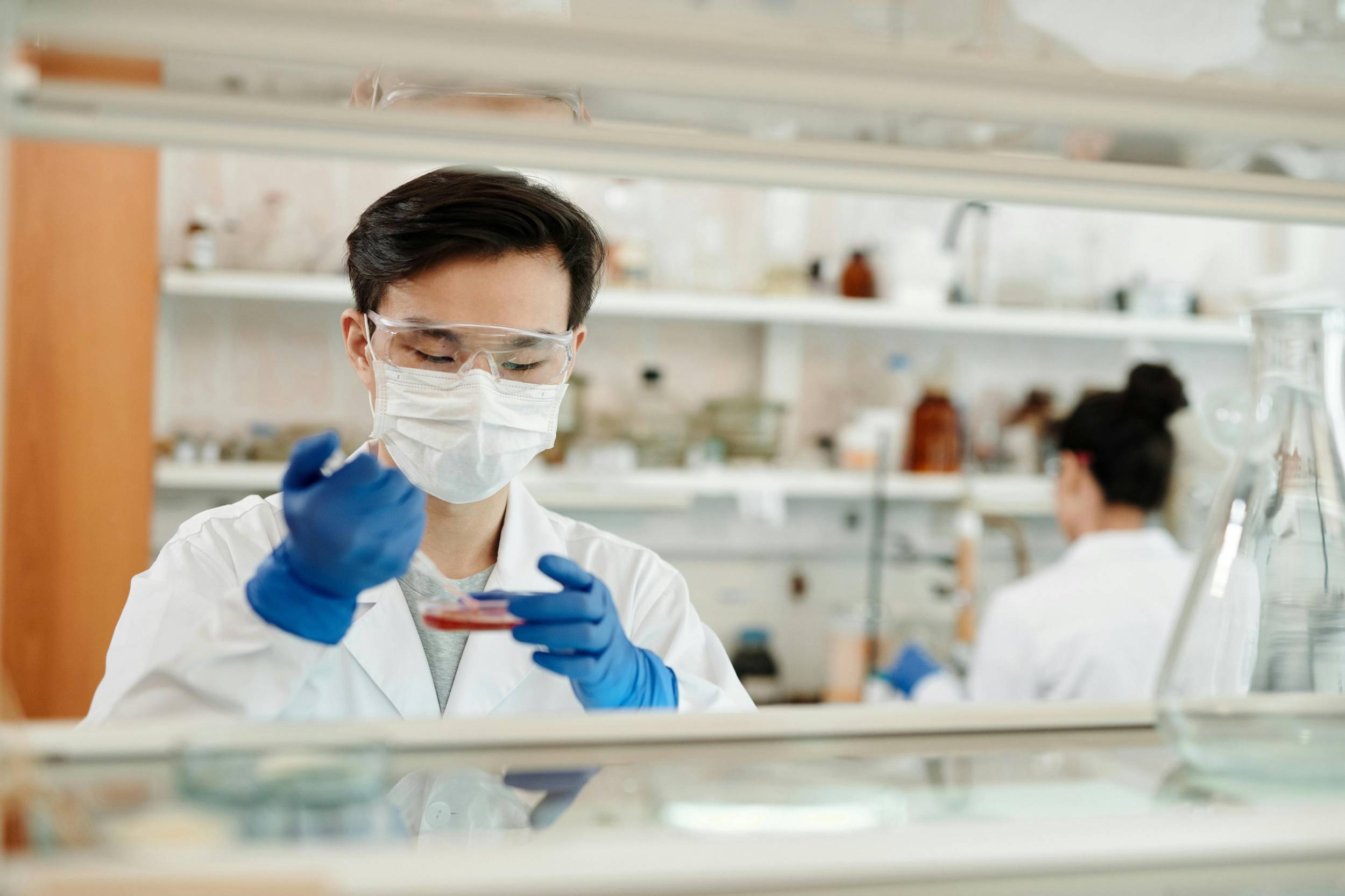 a masked pharmacist placing liquid in petri dish