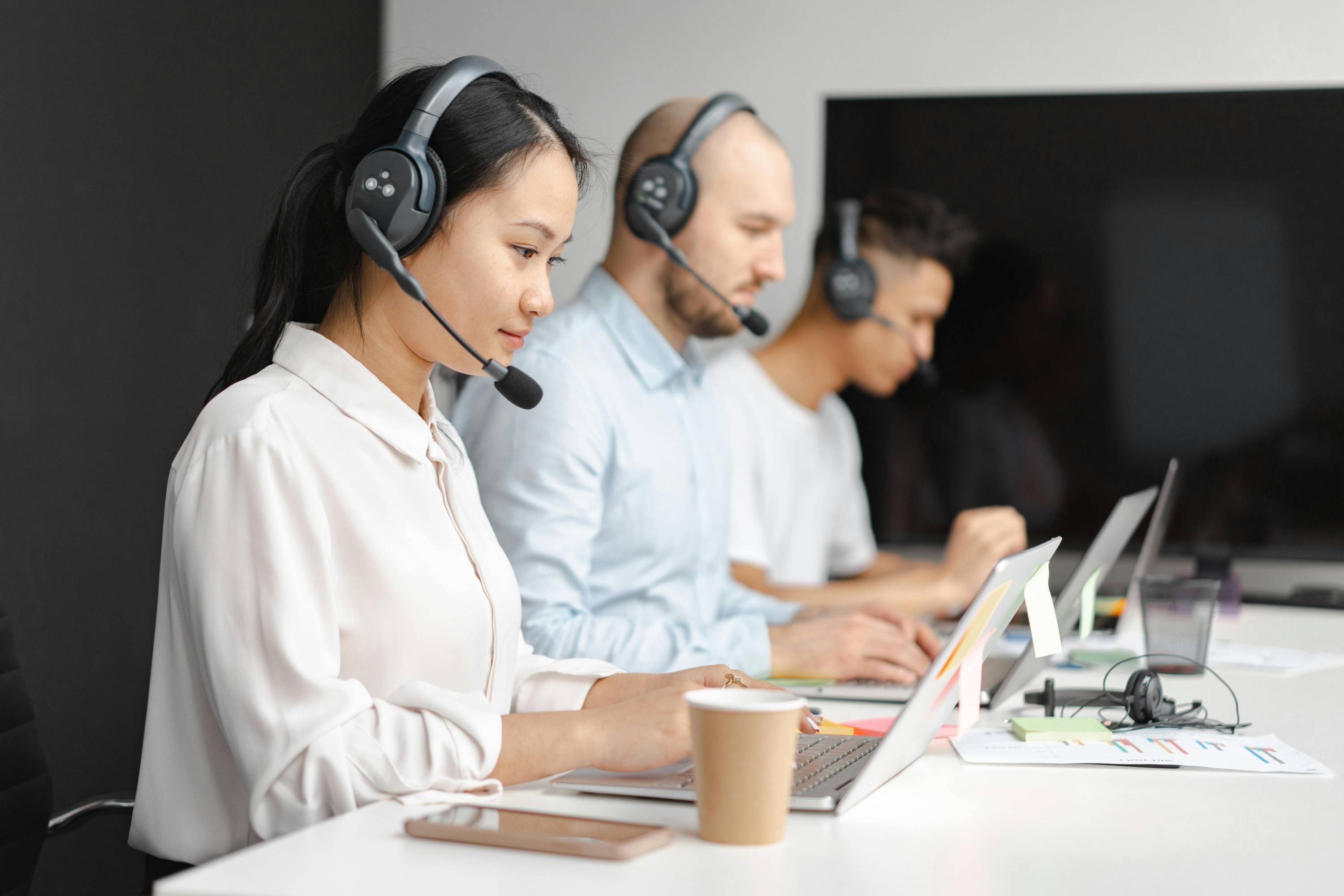 three people on headsets looking at computer monitors