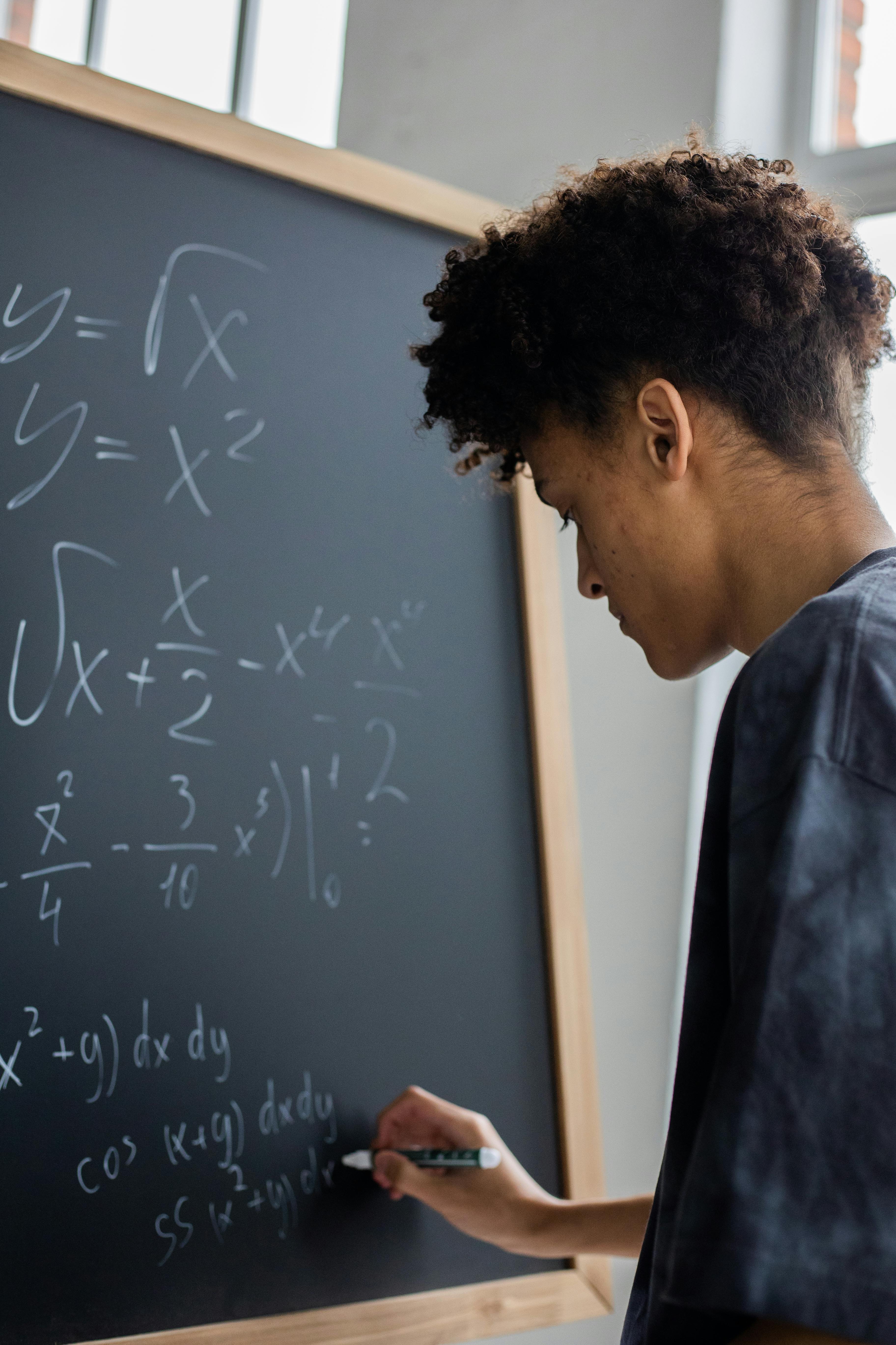 A young boy writing math equations on the board