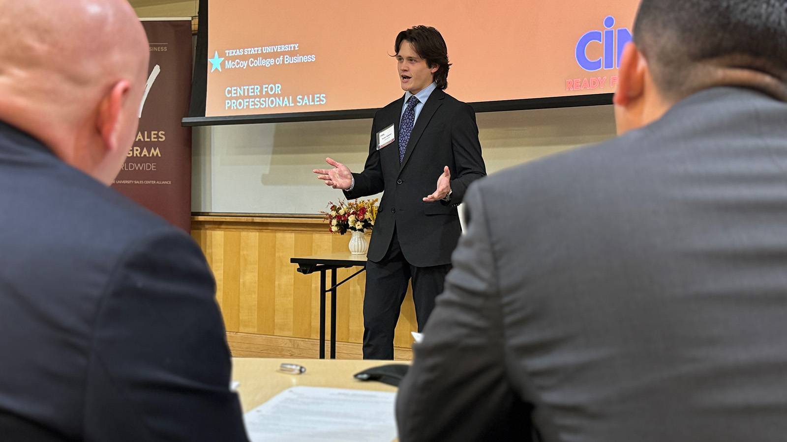 professionally dressed male student standing in front of classroom while speaking to audience