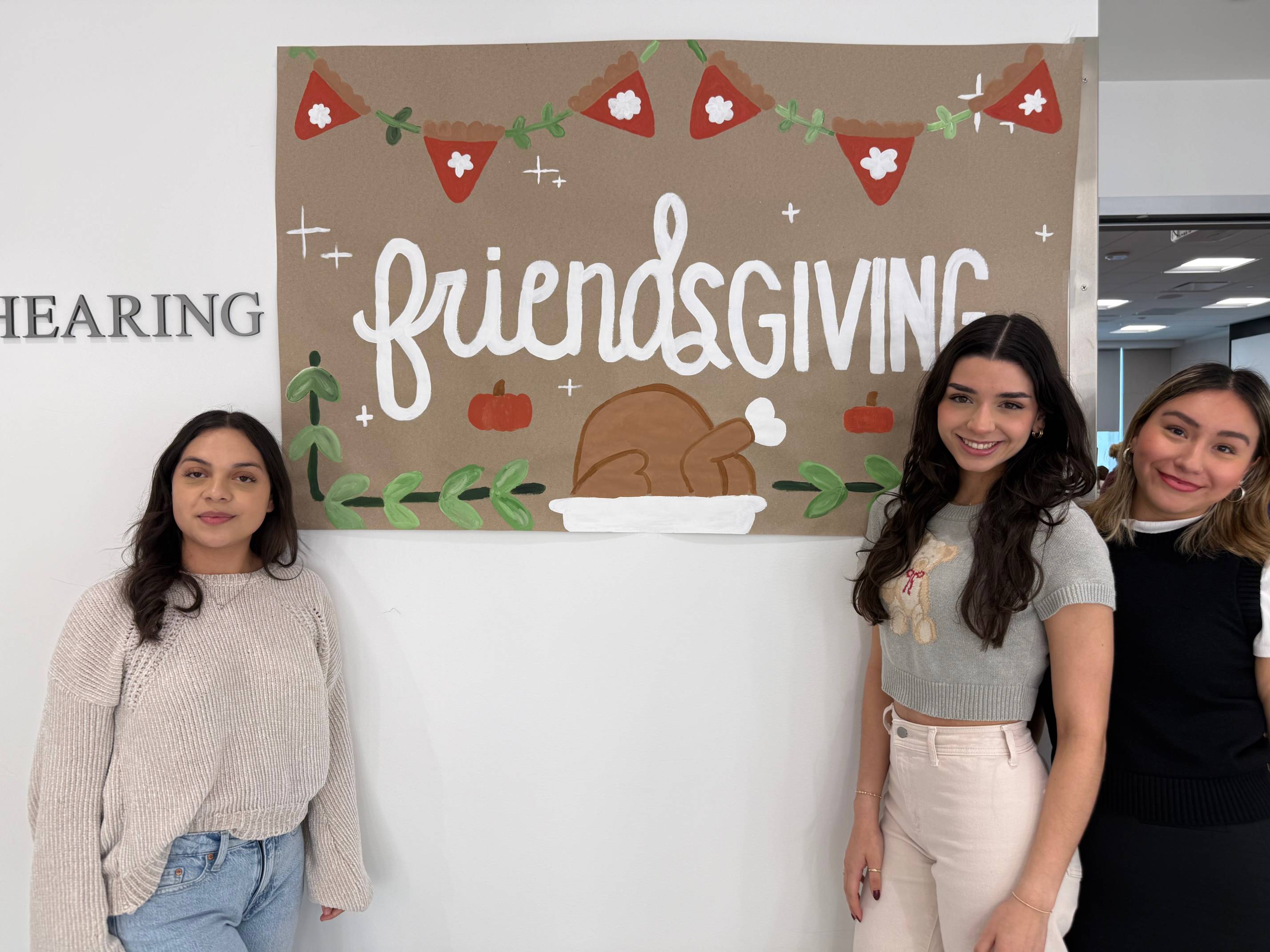 CDIS students posing next to the Friendsgiving poster.