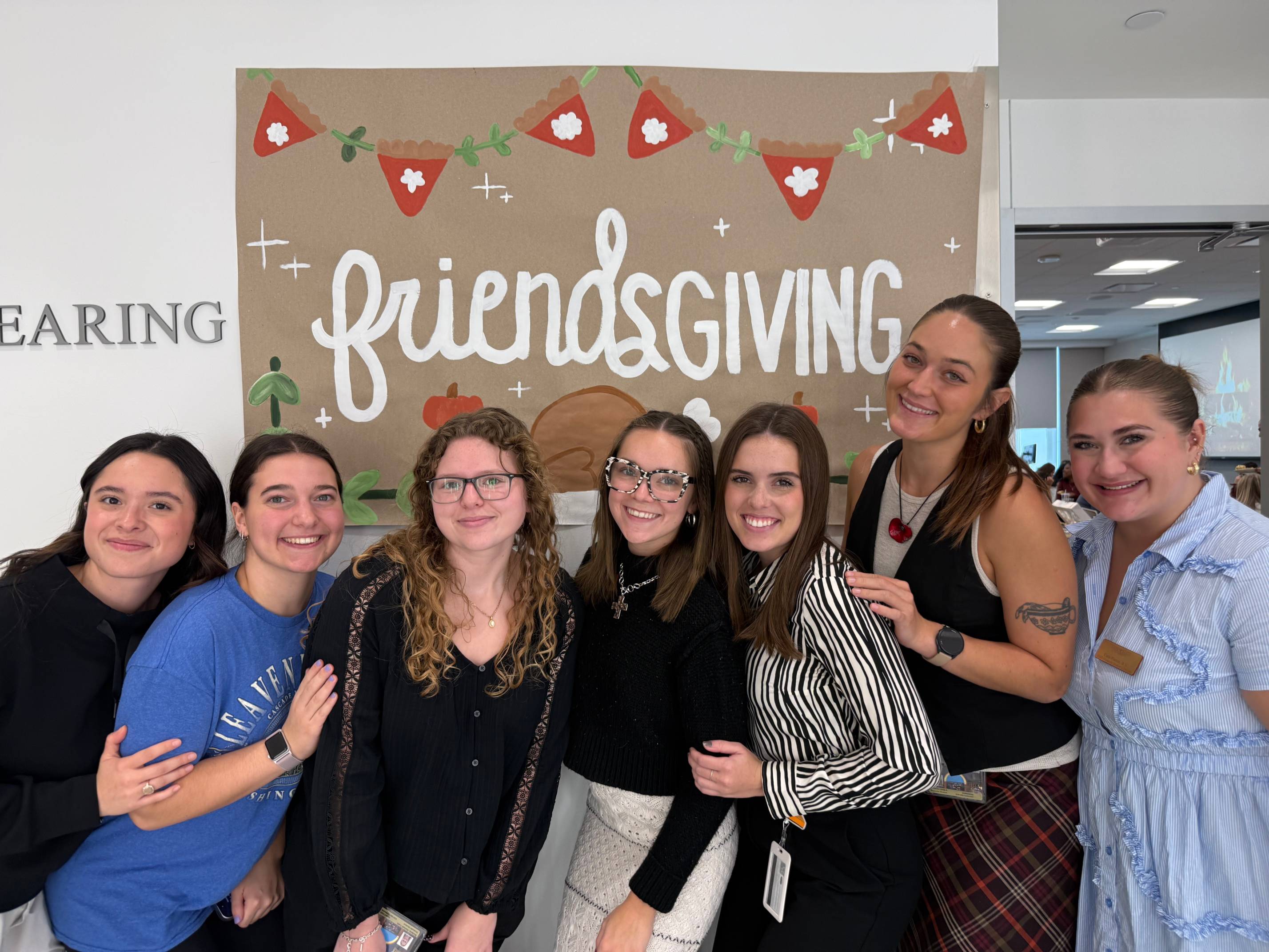 Group of students standing next to the Friendsgiving poster.