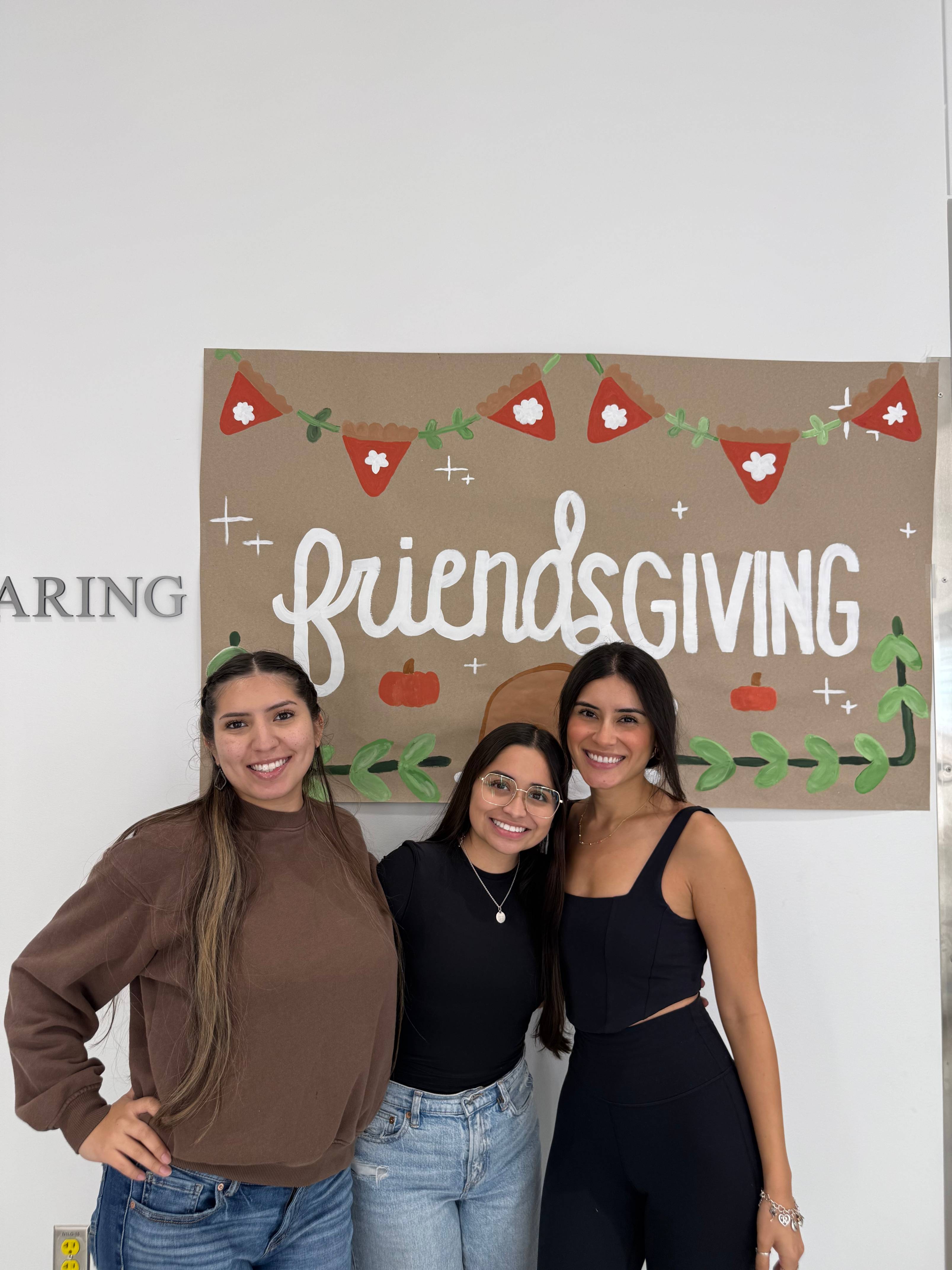 CDIS students posing next to the Friendsgiving poster.