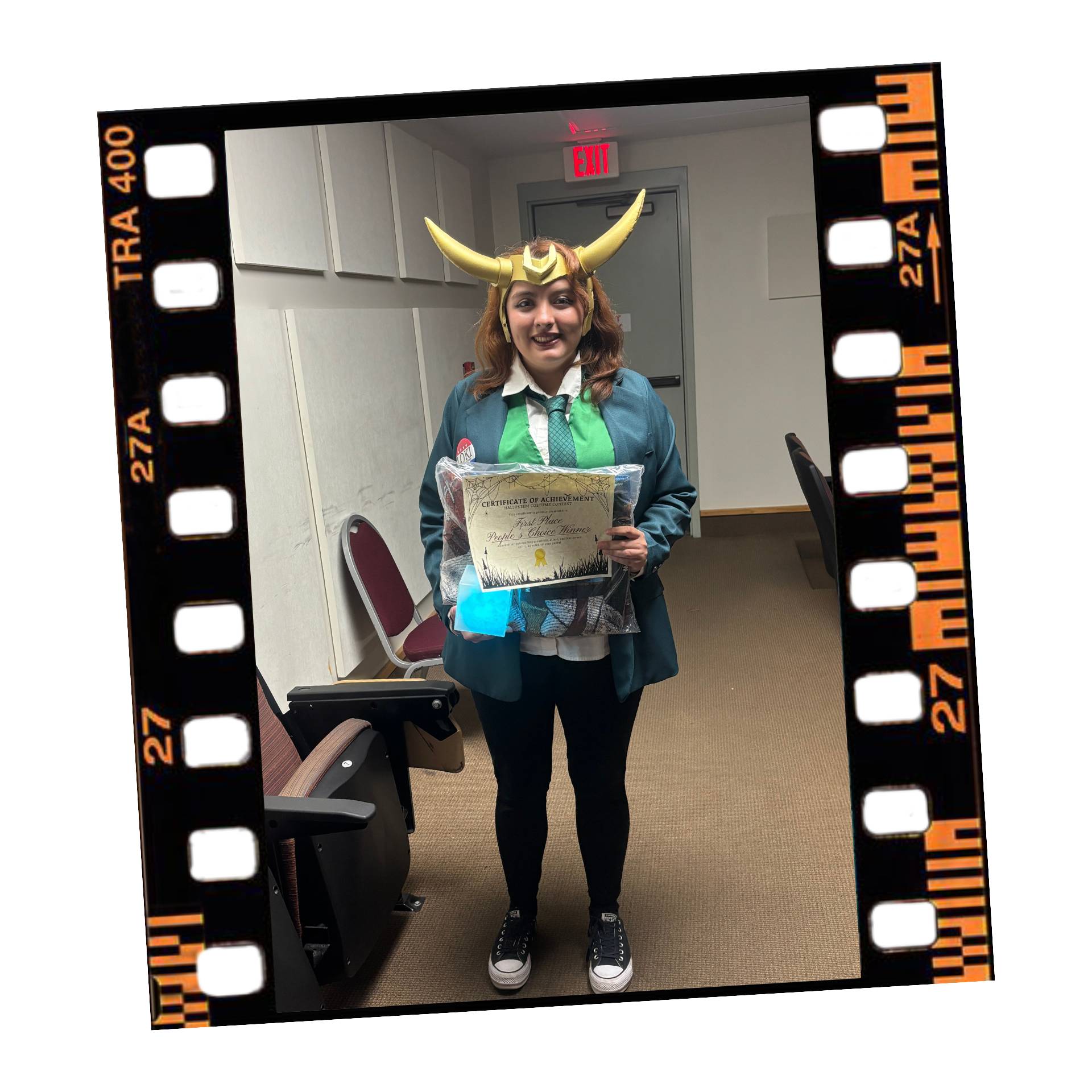 A person dressed in a Loki-inspired costume, featuring a green blazer, a tie, and a horned helmet, stands indoors holding a Certificate of Achievement. The image is framed within a simulated film strip border.