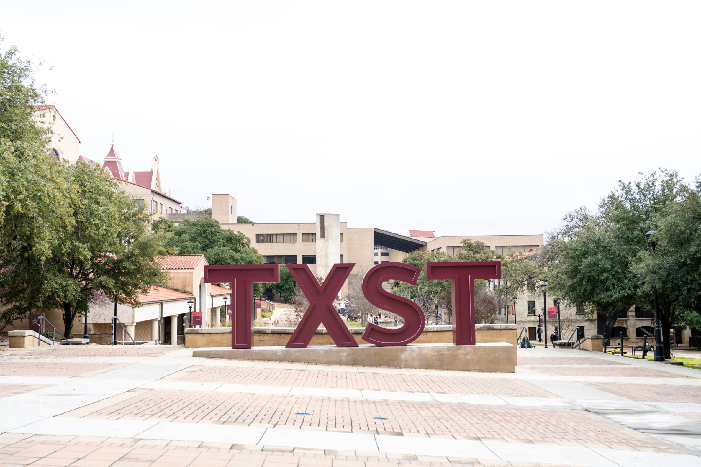 txst logo in maroon with the campus in the background