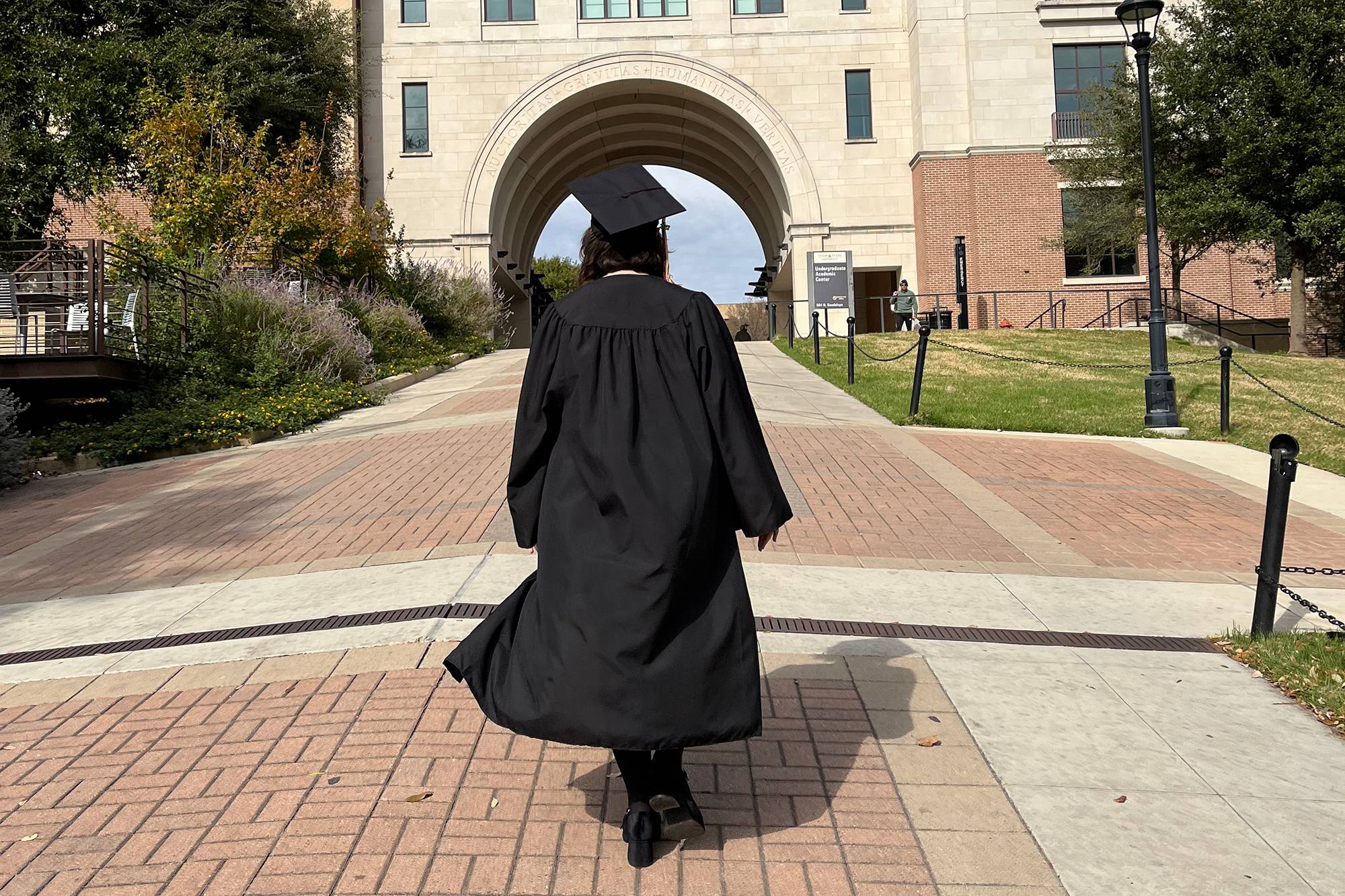 Abby Parker walking towards the arches in her regalia on the San Marcos campus