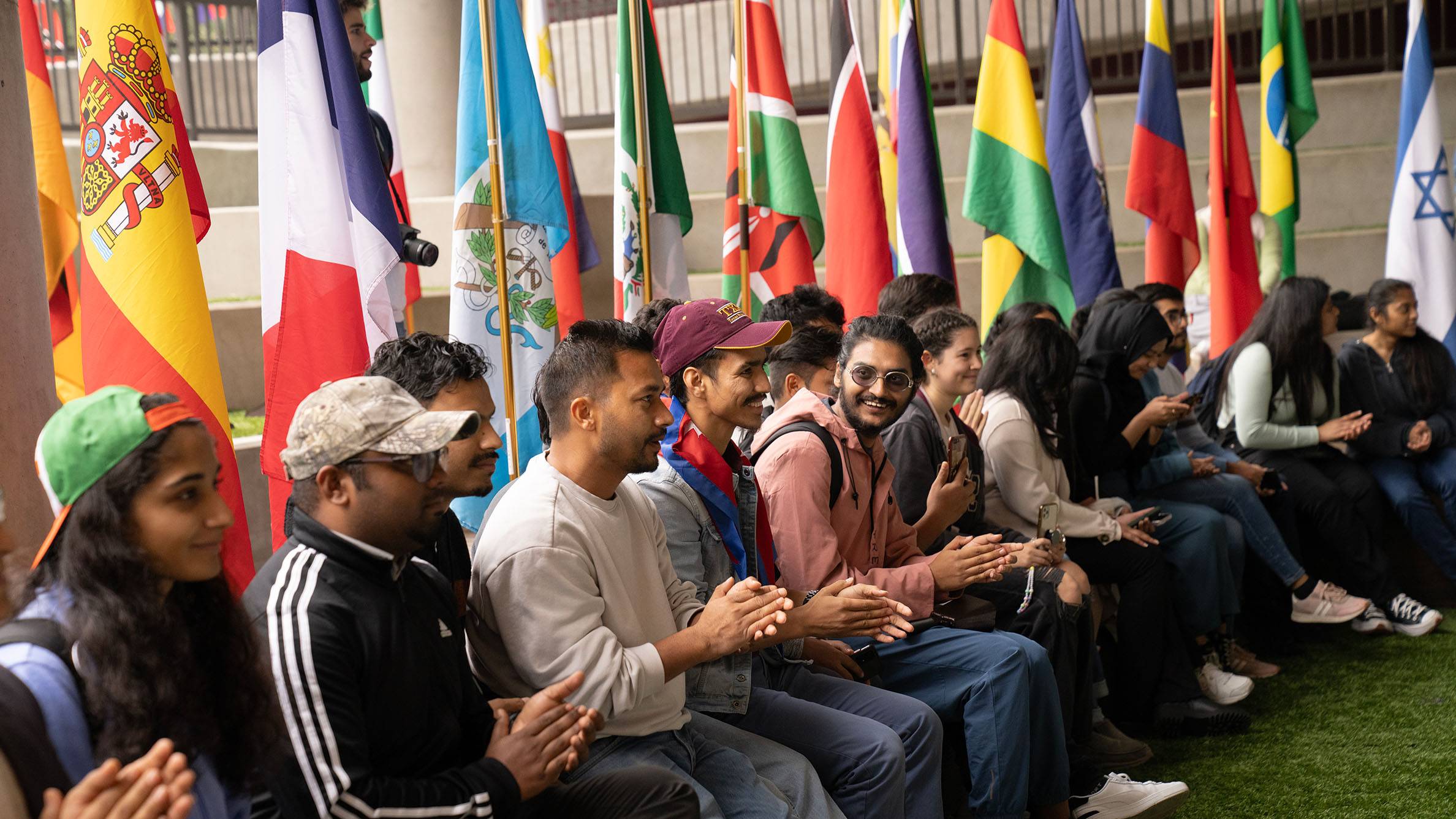 A group of students sit near flags at an event.