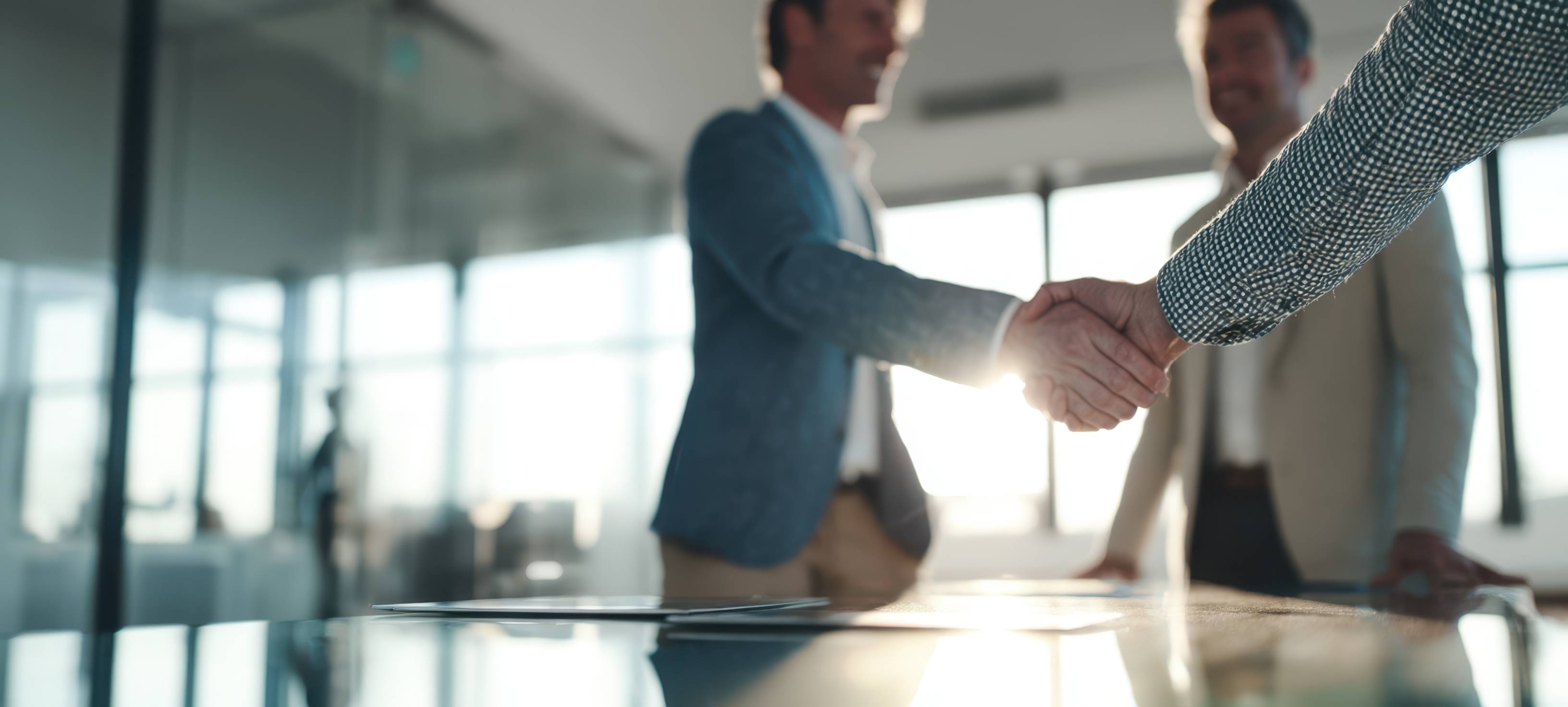 two men in a conferencre room shaking hands in front of a third man