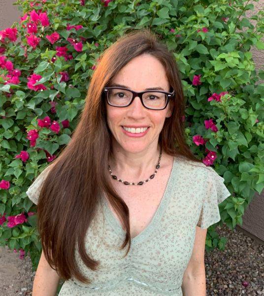 woman standing in front of a bush with green dress and black glasses