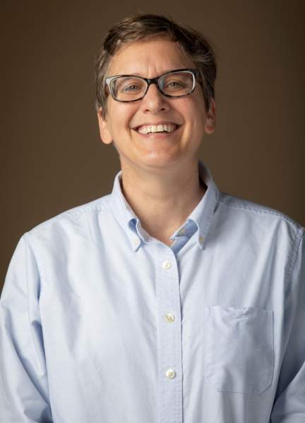 woman with short hair wearing a light blue button up shirt smiling at camera