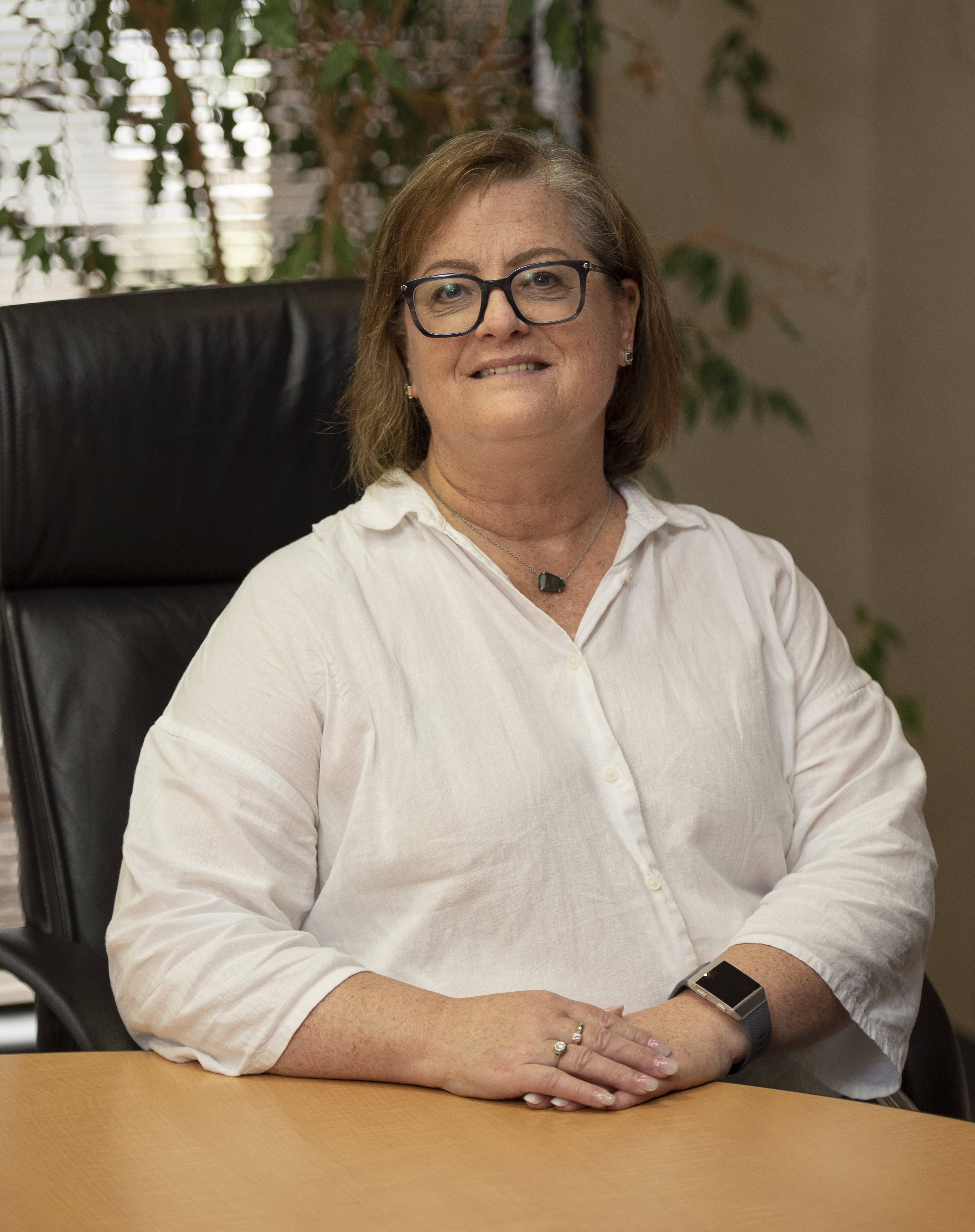 woman wearing glasses and white button up shirt sitting behind desk and smiling at camera