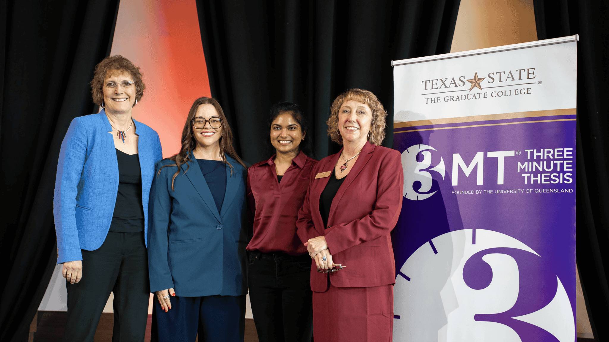 Two deans and two competitors next a 3MT banner