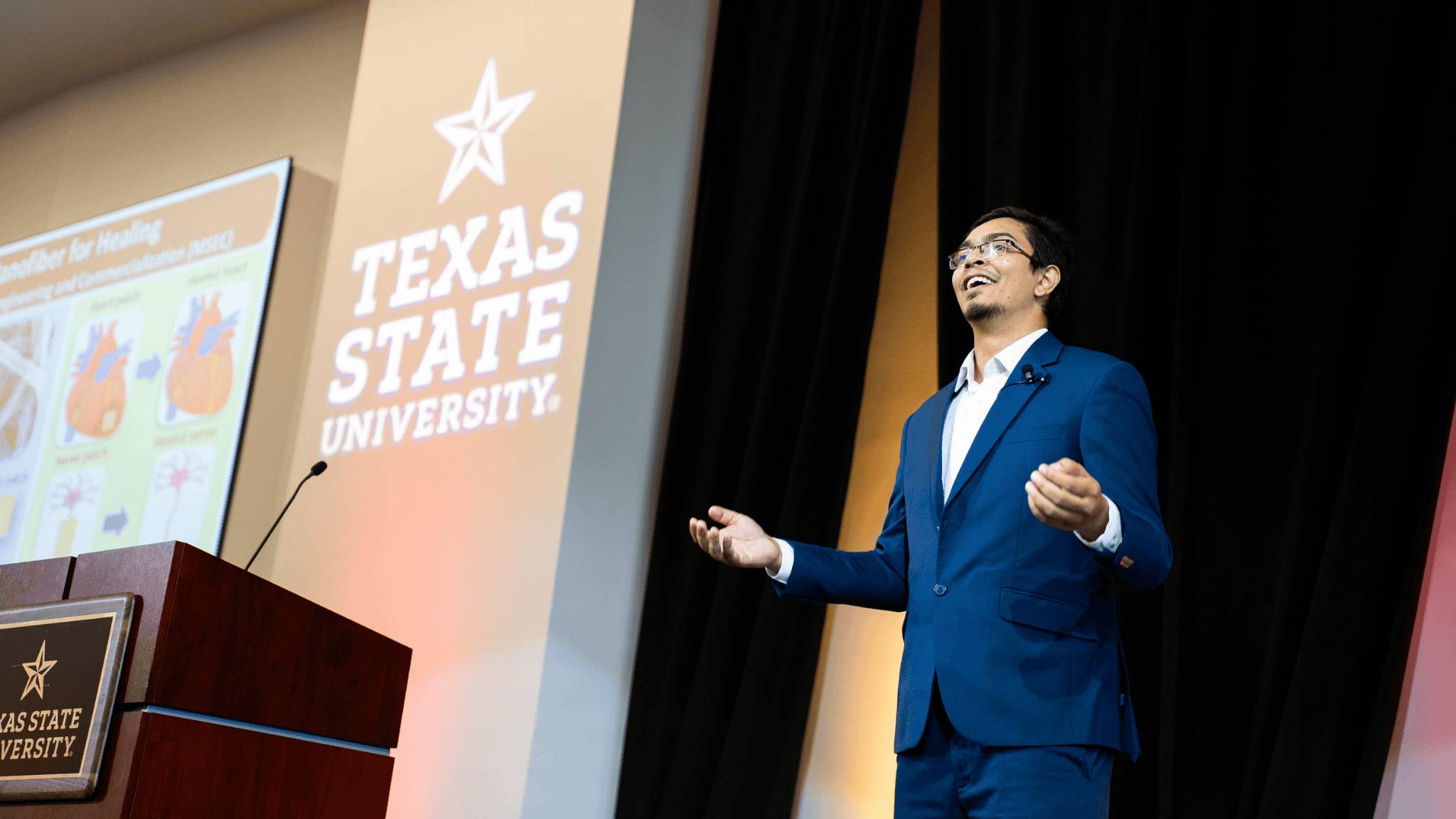 a male student giving a pesentation to a conference room full of people