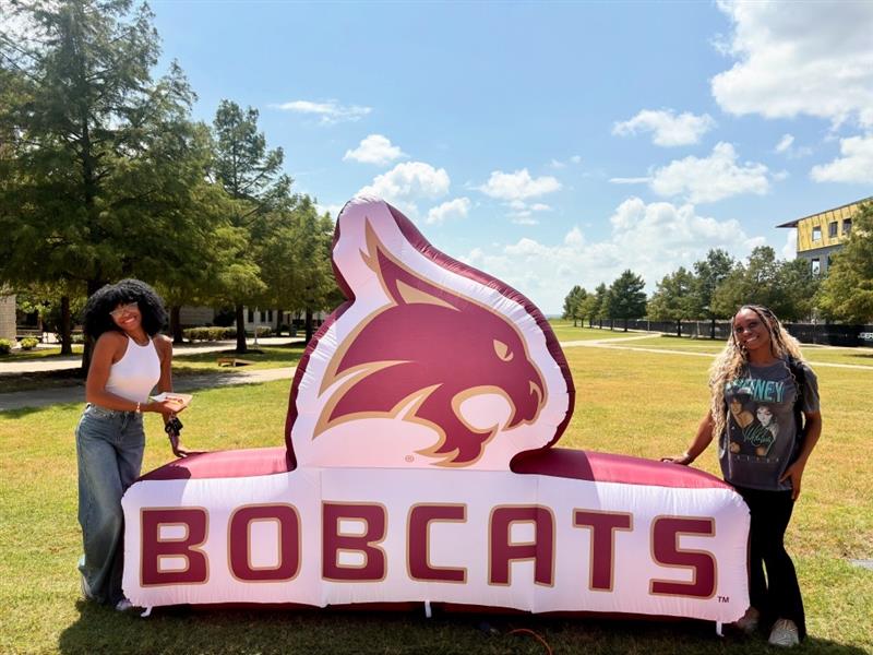 two people standing by a balloon with the txst bobcat logo