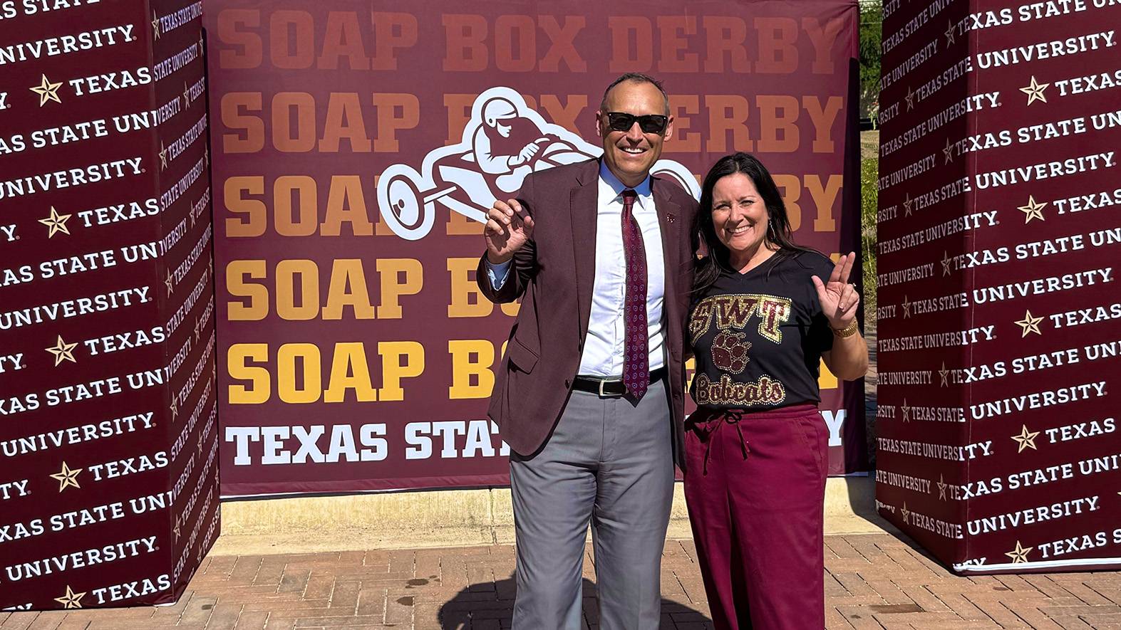 President Damphousse (left) and First Lady Beth Damphousse pose for a photo in front of the Soap Box Derby sign.