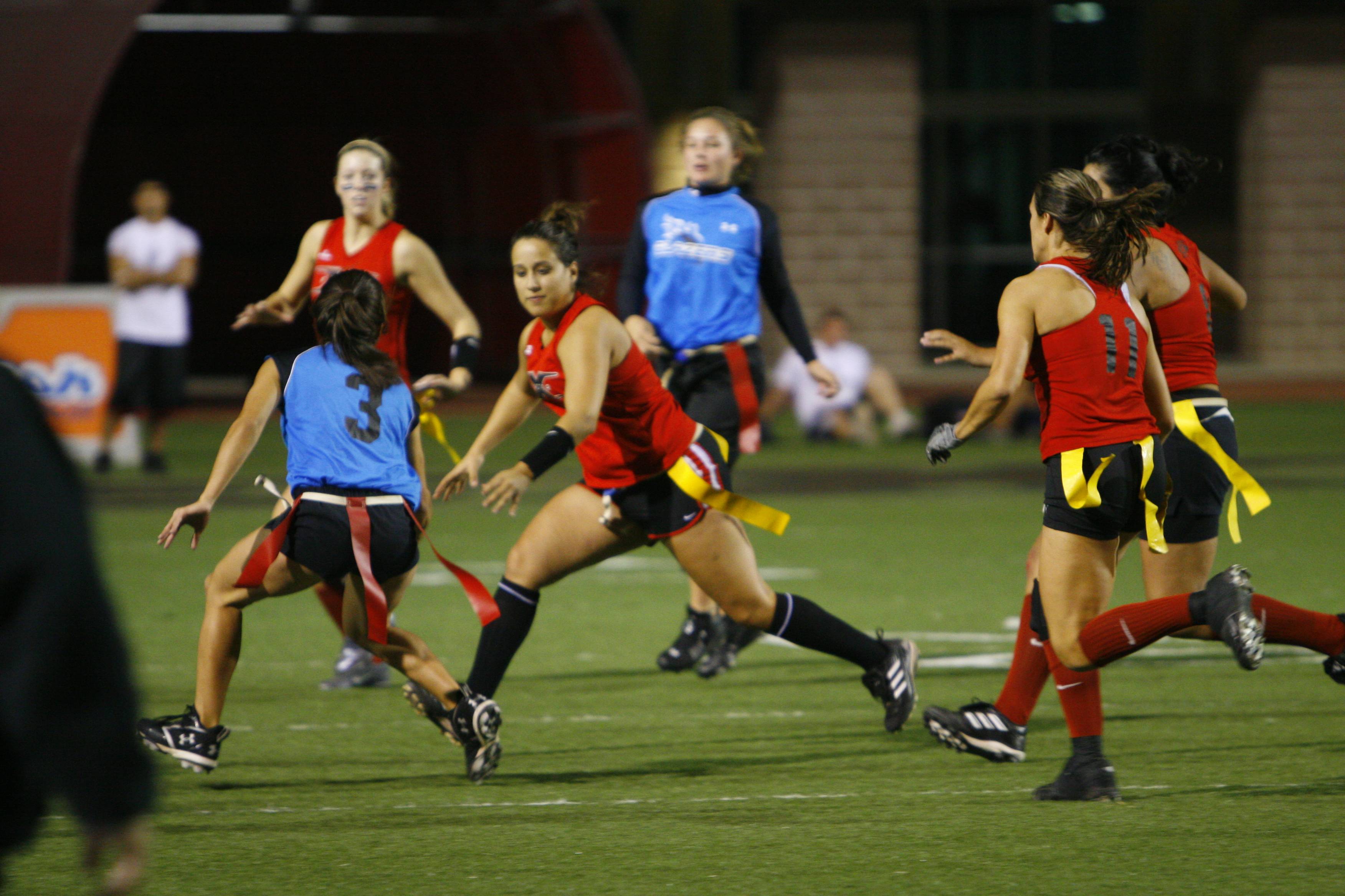 flag football participants running the football to the endzone while defenders attempt to pull flag