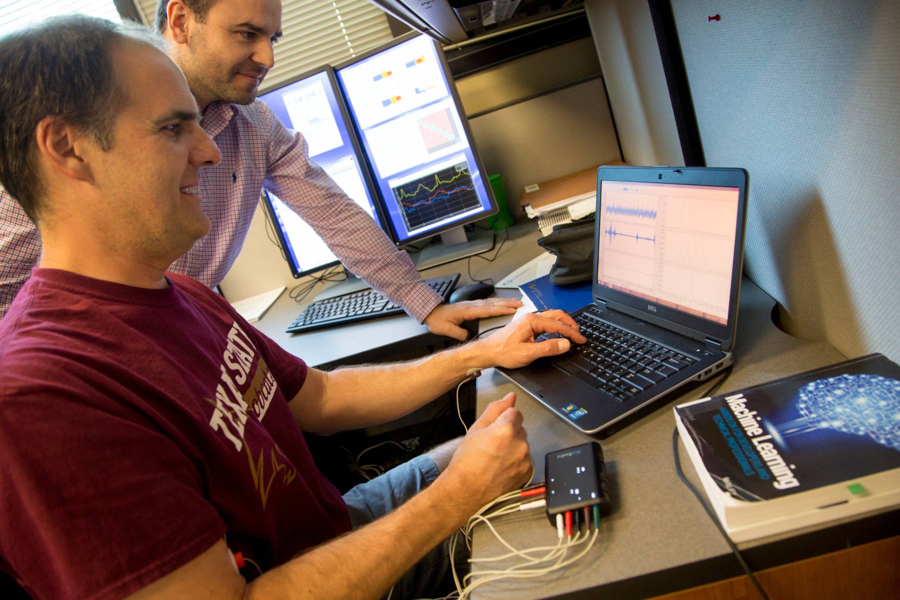 A student and a professor sitting down by a group of computers and programming.